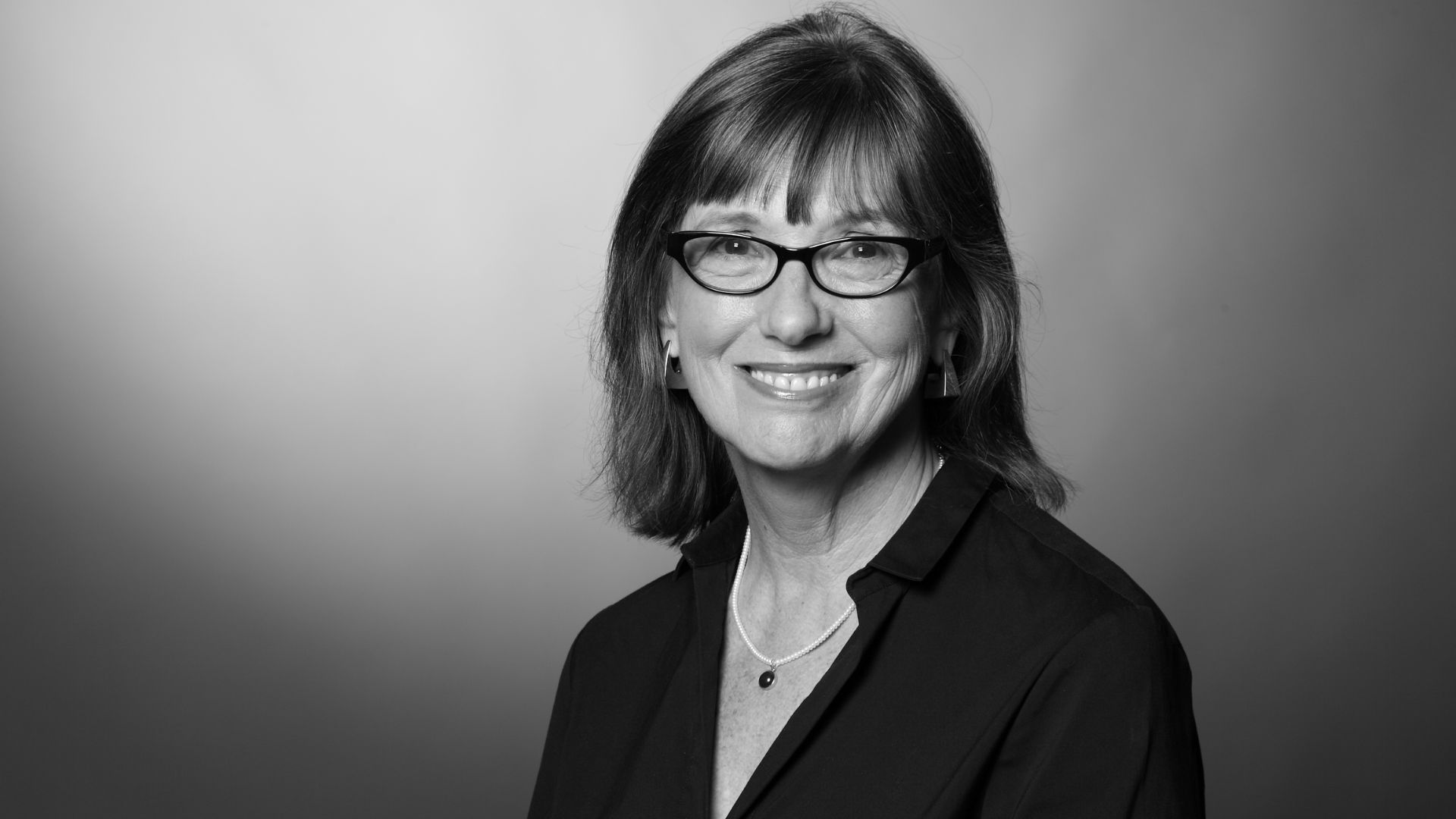 A woman wearing glasses and a black shirt smiles warmly at the camera.
