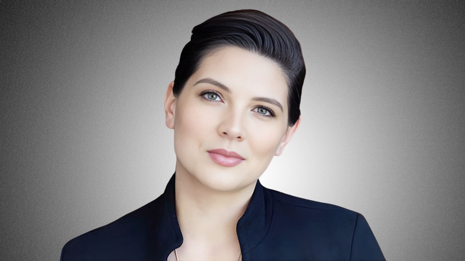 A woman with short hair wearing a black jacket stands confidently, showcasing a modern and professional appearance.