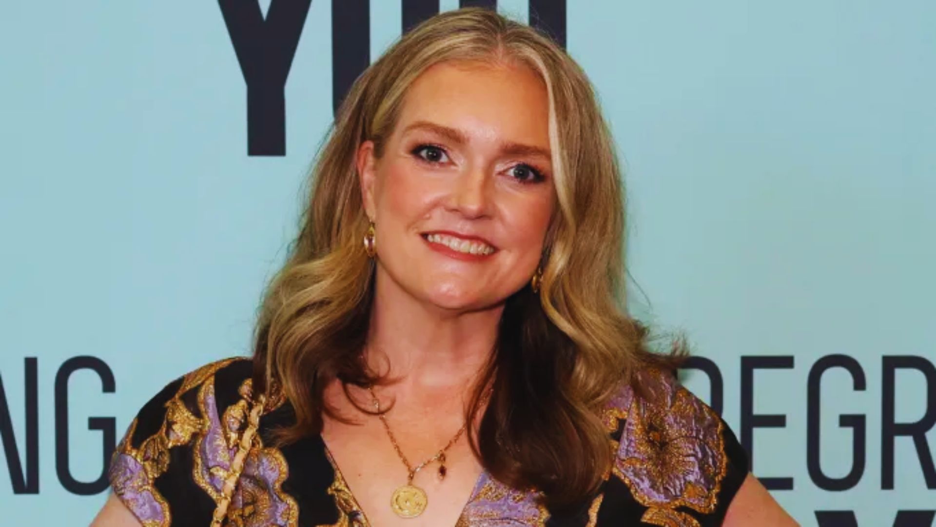 A woman in a floral dress poses elegantly on a red carpet.
