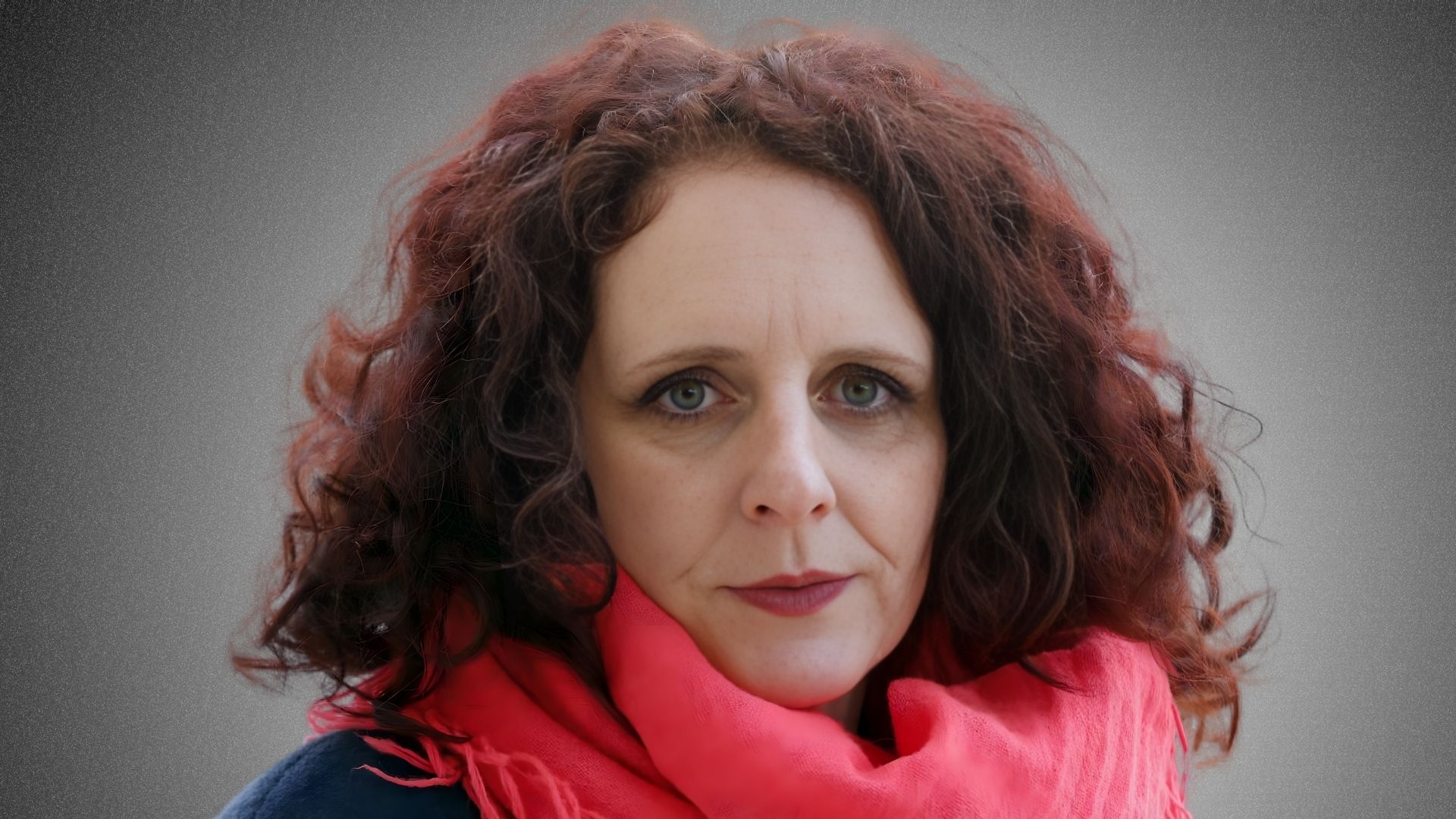 A woman with red hair wearing a pink scarf, smiling softly against a neutral background.