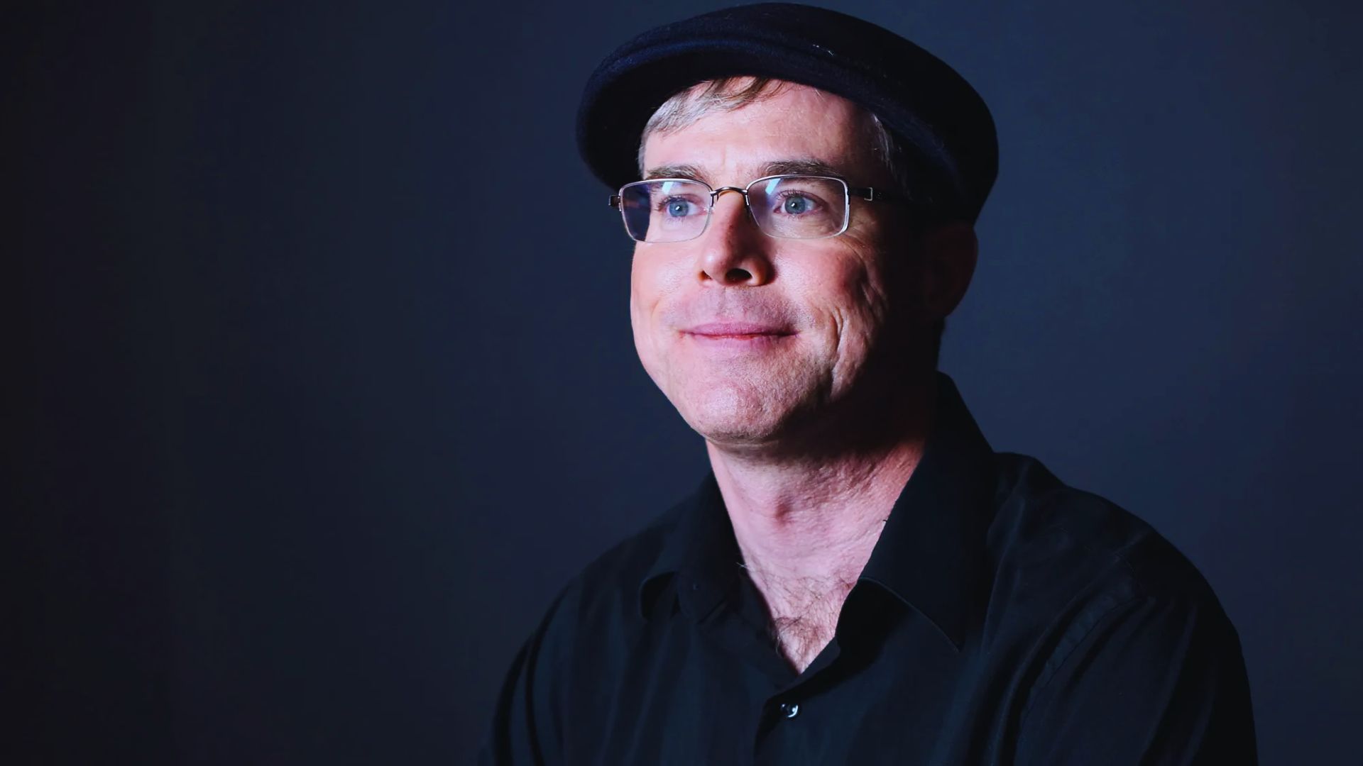 A cheerful man named Andy Weir, wearing glasses and a hat, smiles at the camera.