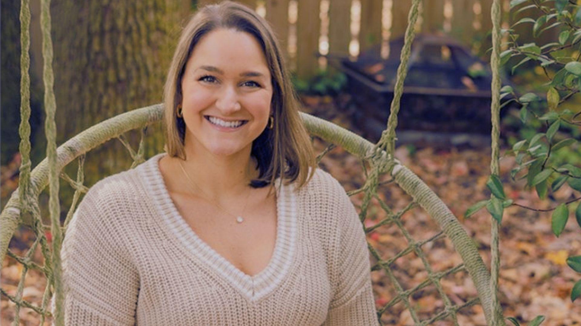A woman sitting on a swing surrounded by colorful autumn leaves in a serene fall setting.