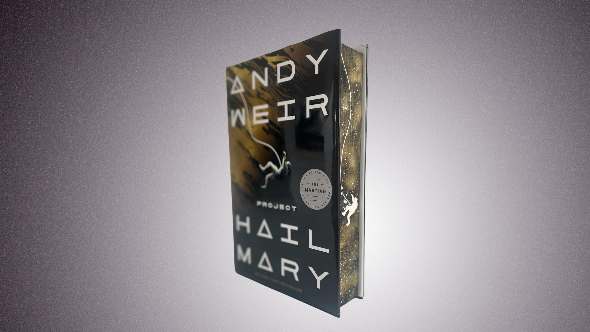A book titled "Project Hail Mary" by Andy Weir placed on a table, set against a black backdrop.