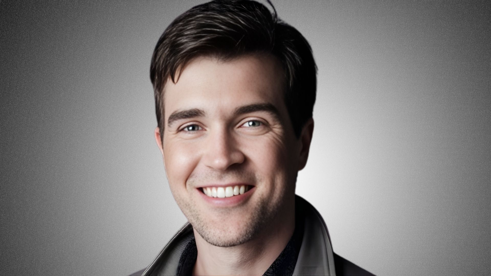 A man in a gray jacket smiles warmly at the camera.