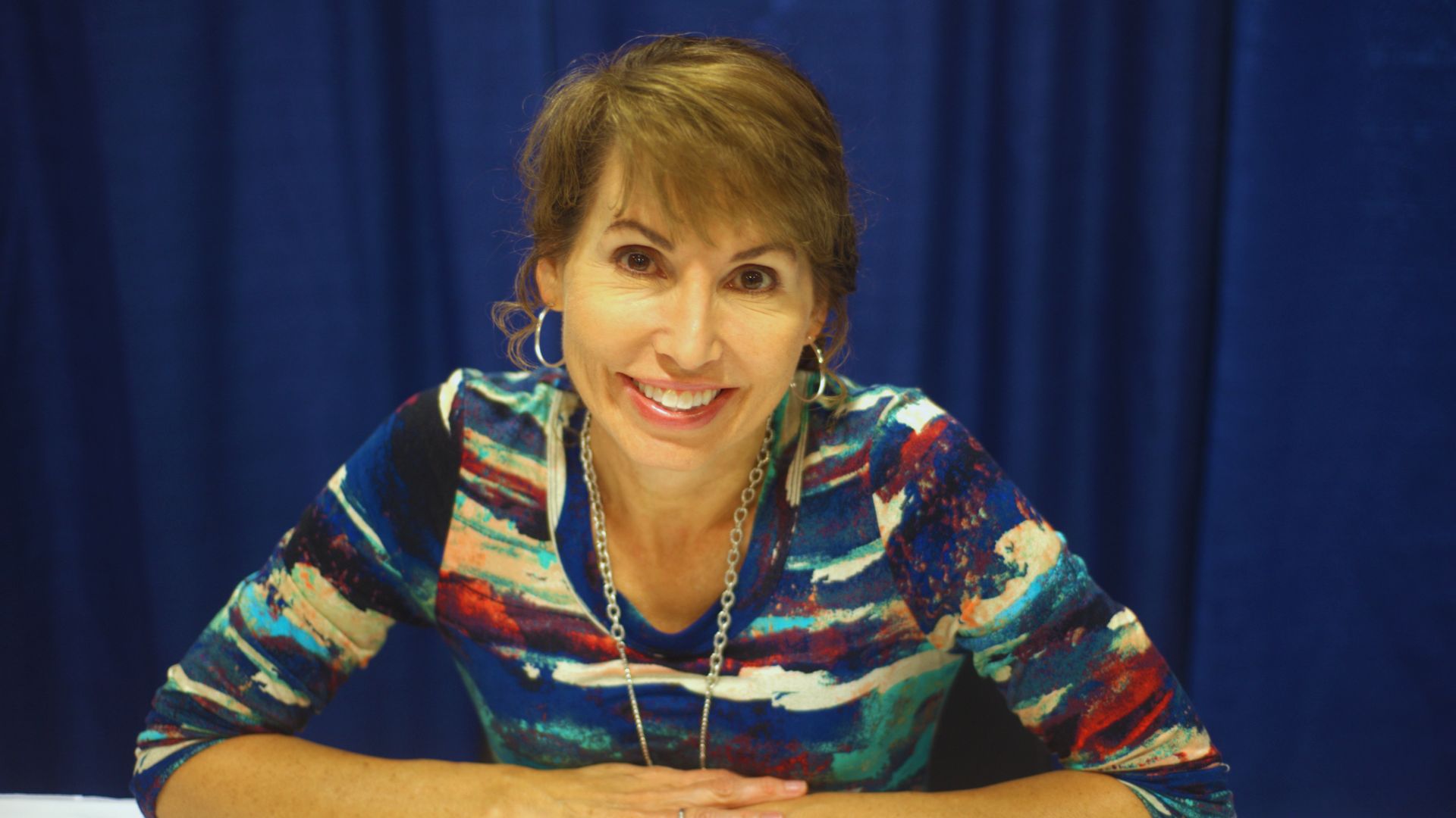 A smiling Lisa Wingate sits at a table, embodying her dedication to writing historical and inspirational fiction.