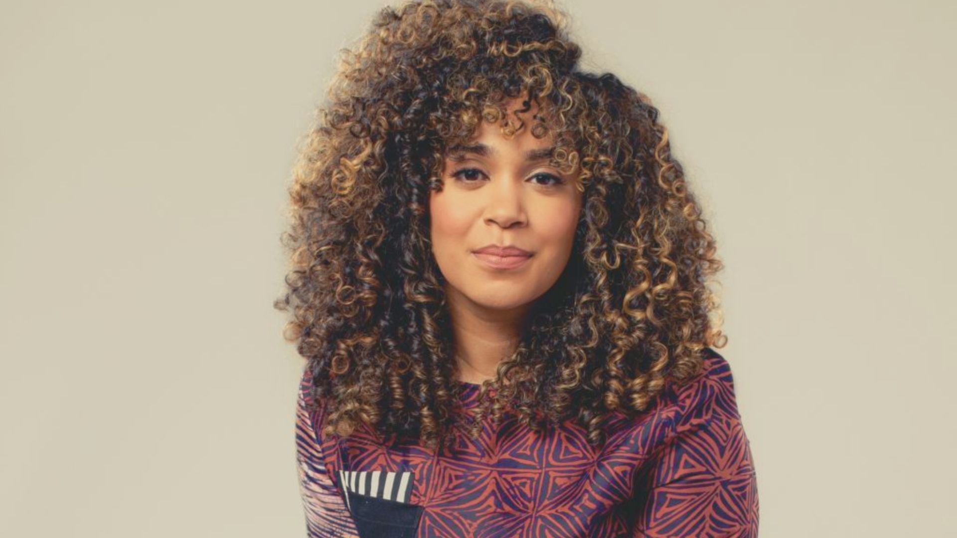 Elizabeth Acevedo, a Dominican-American poet, with curly hair and a vibrant shirt, known for her impactful verse novels.