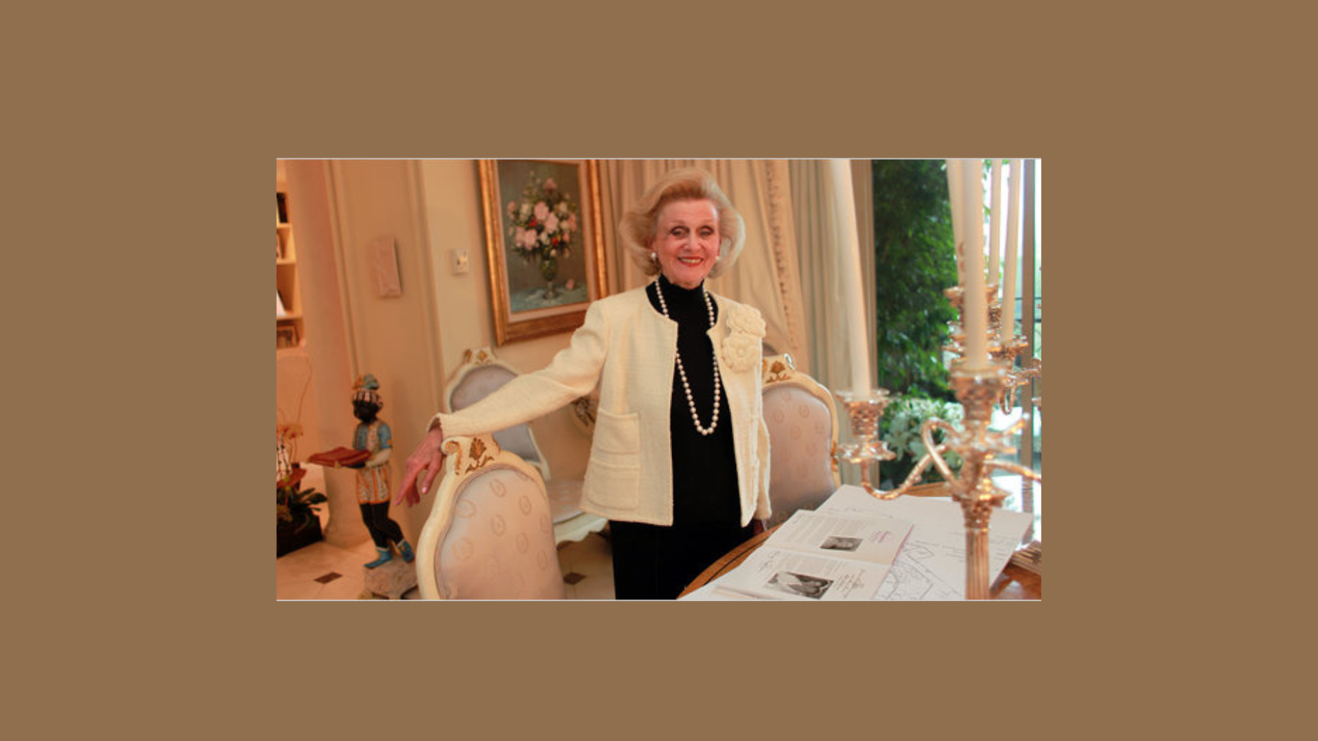 A woman in a white jacket stands beside a table, looking confidently at the camera.