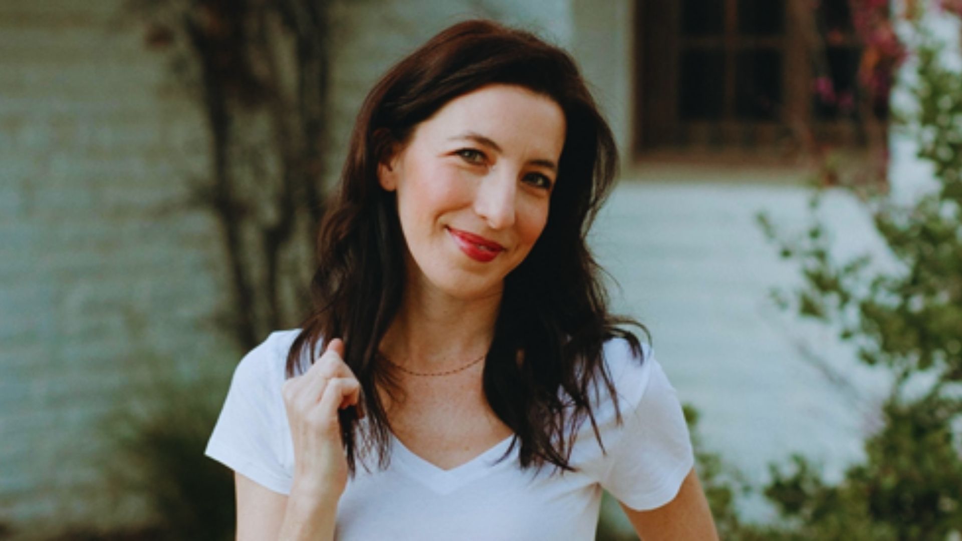 A woman in a white shirt poses for a photo, smiling confidently at the camera.