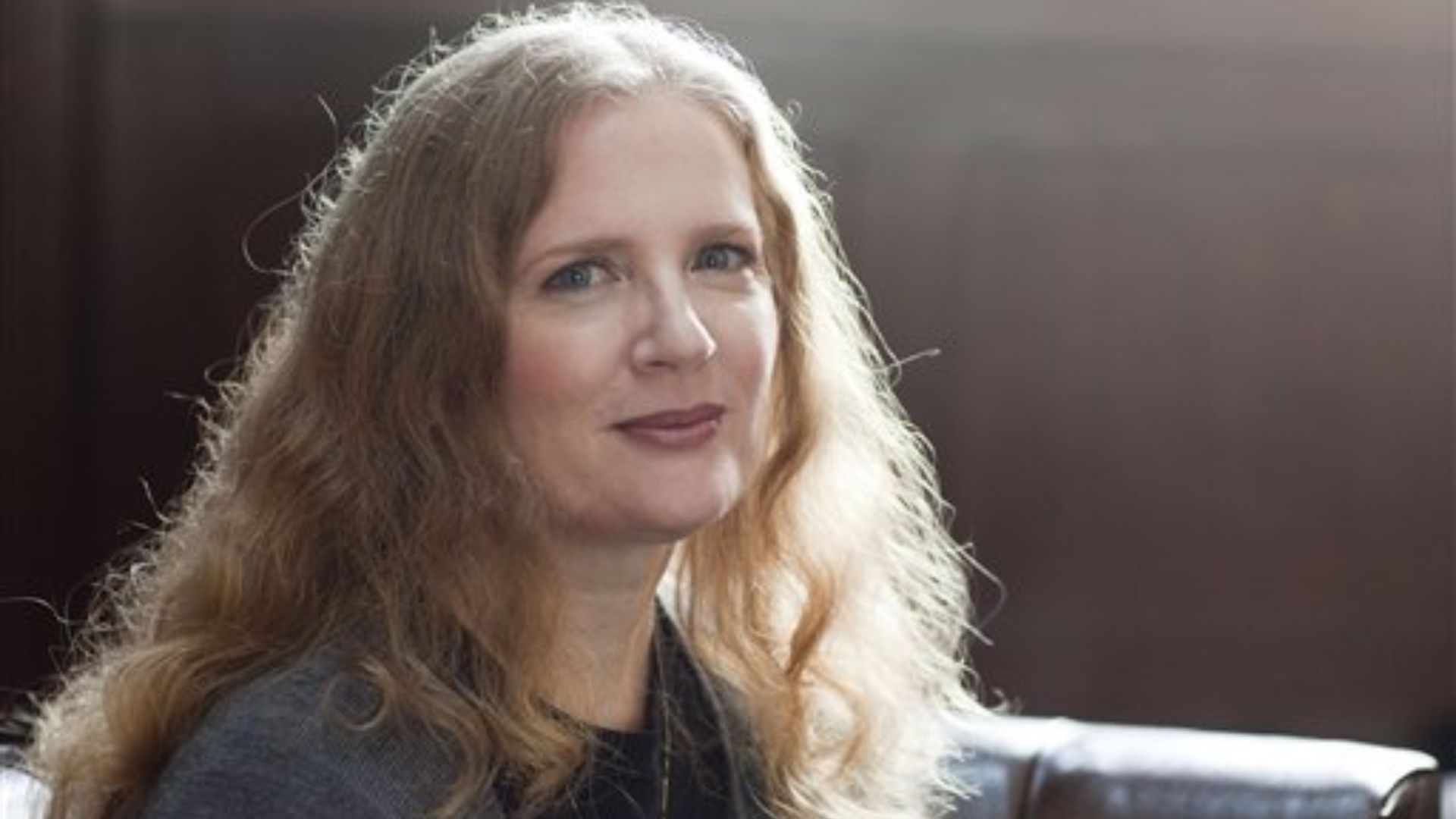 A woman with long hair is sitting comfortably on a couch, looking relaxed and engaged in her surroundings.