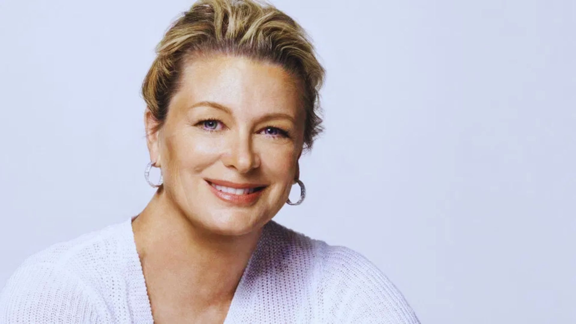 A woman with short blonde hair smiles warmly, radiating happiness and approachability.