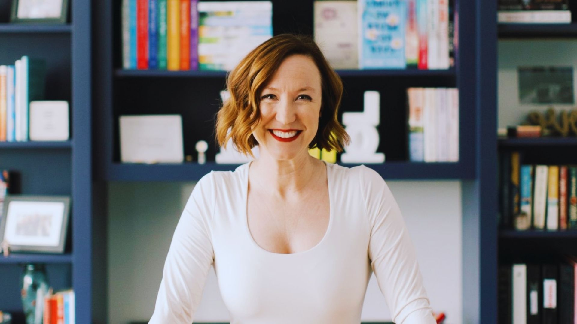 A woman in a white shirt sitting at a desk, focused on her work with a laptop and notepad in front of her.
