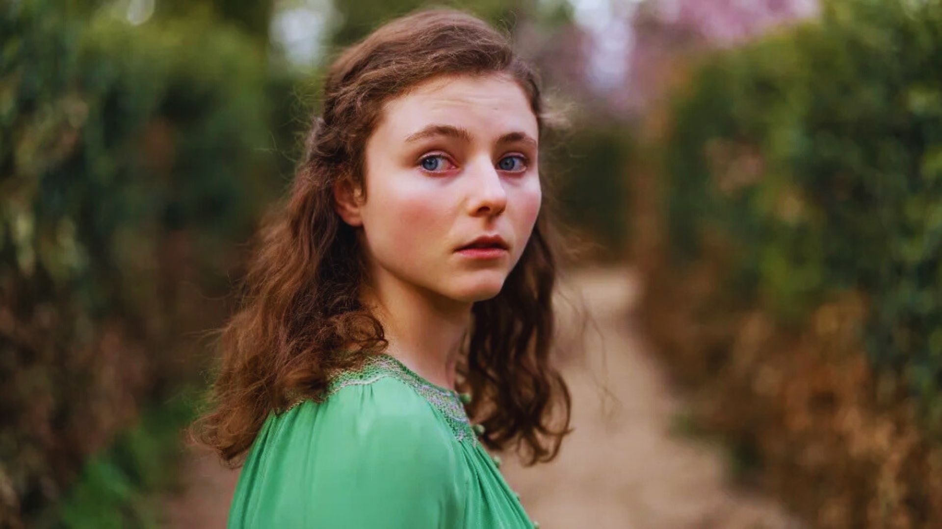 A young woman with long hair wearing a green dress smiles while looking directly at the camera.