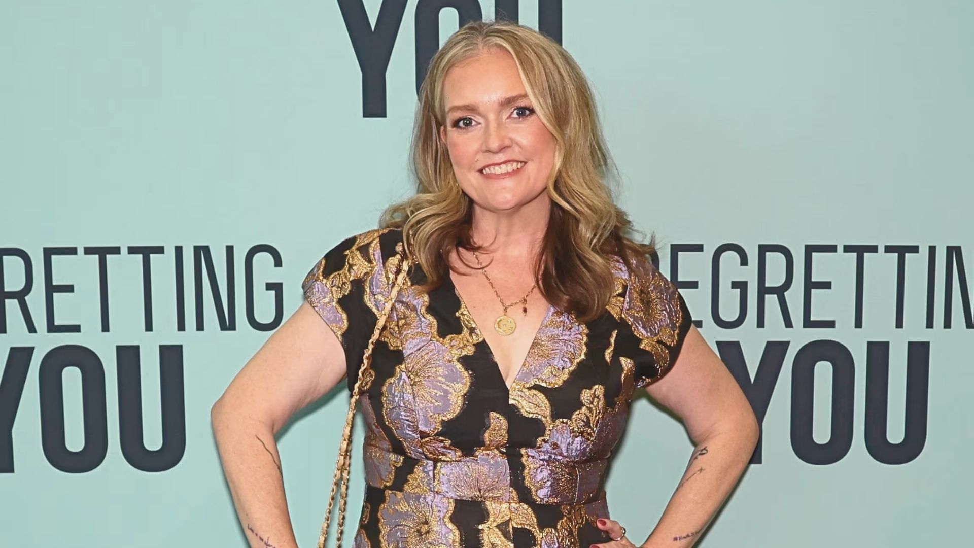 A woman in an elegant dress poses for a photo at a film premiere, smiling confidently at the camera.