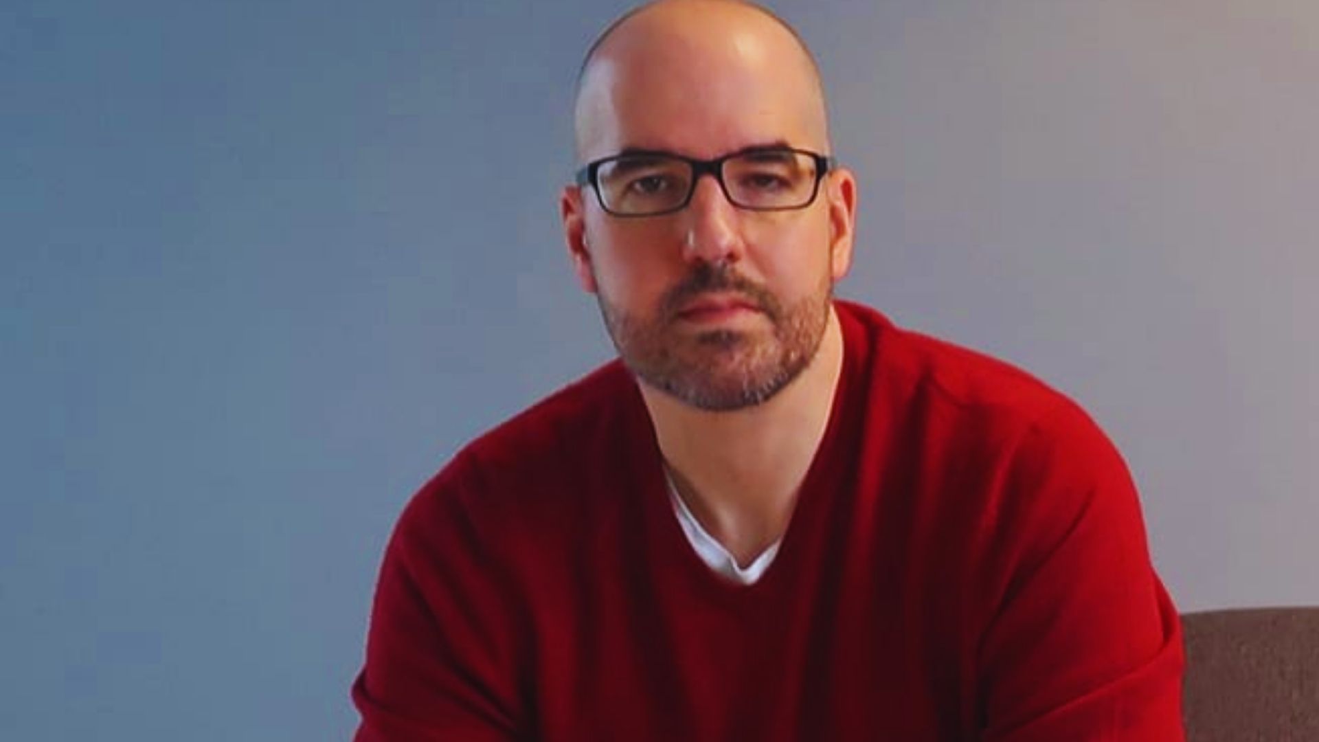 A bald man with glasses sits at a computer, focused on the screen in a well-lit office environment.