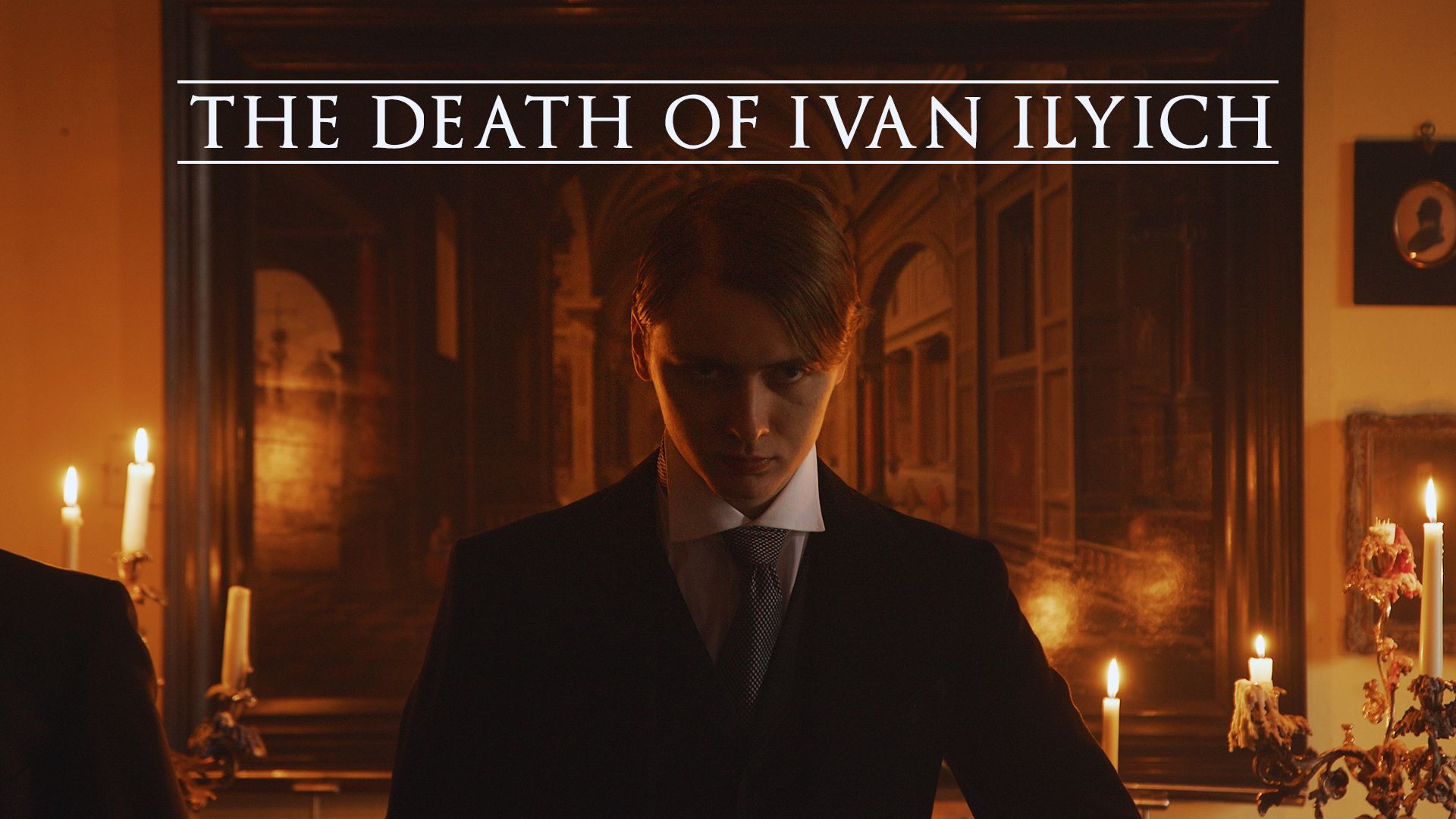 Dark, dramatic scene from "The Death of Ivan Ilyich." A solemn individual in formal attire stares intensely, surrounded by lit candles and a dim, ornate interior.