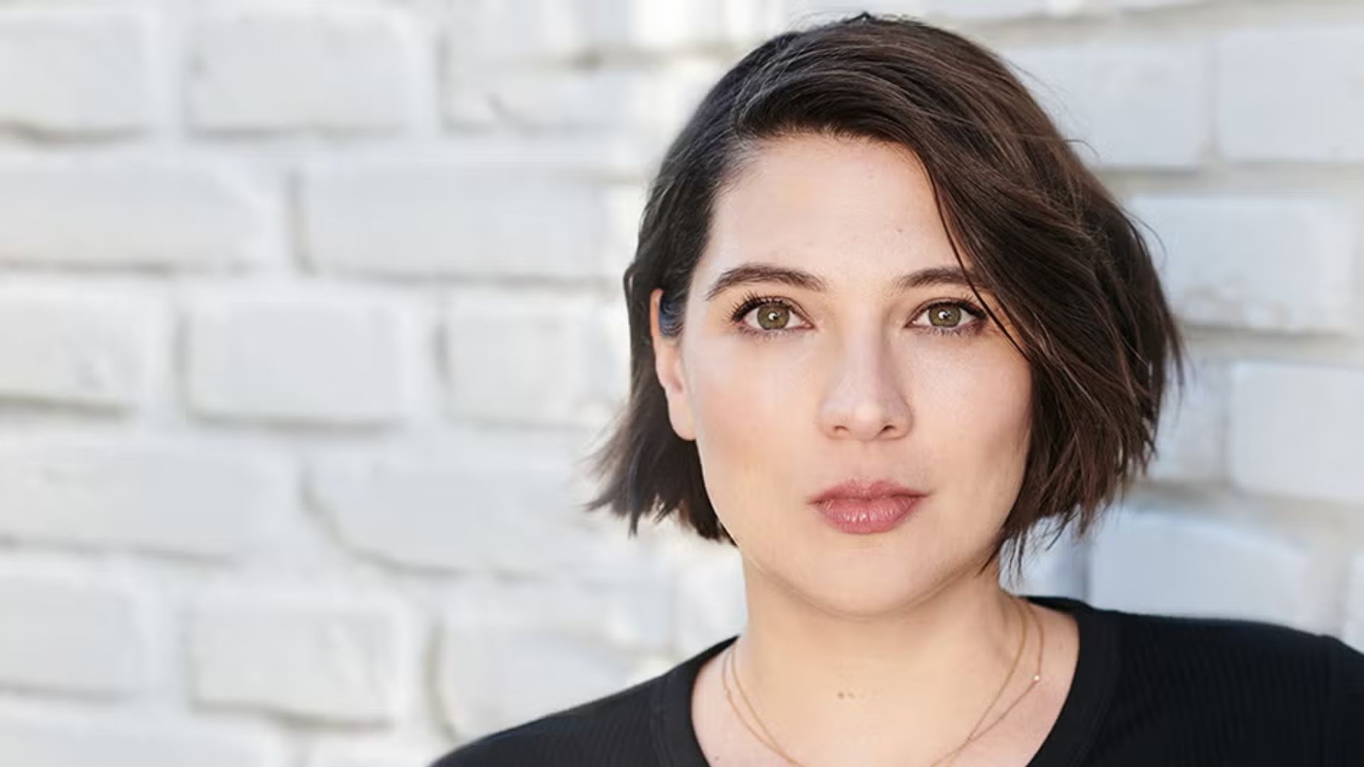 A woman with short hair wearing a black shirt, looking confidently at the camera.