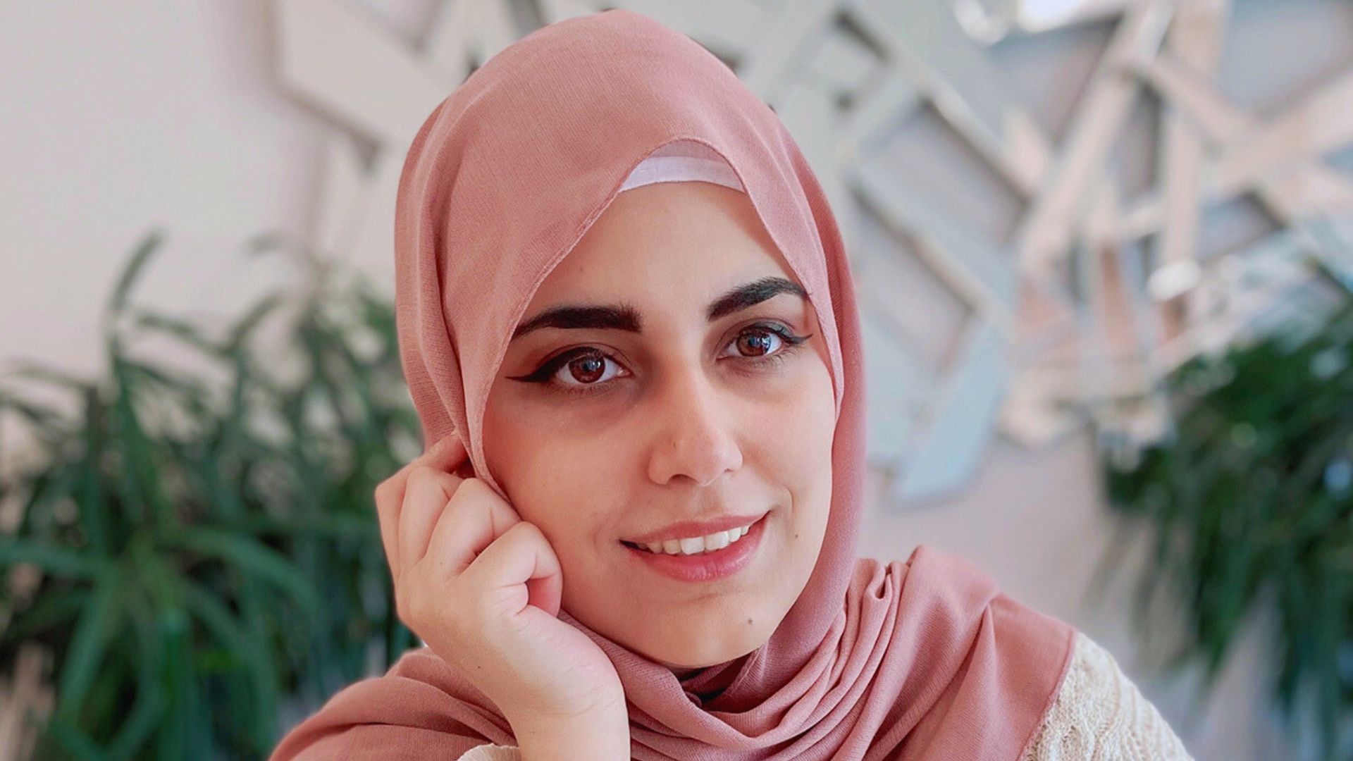 A woman with a pink headscarf smiles warmly at the camera, radiating joy and positivity.