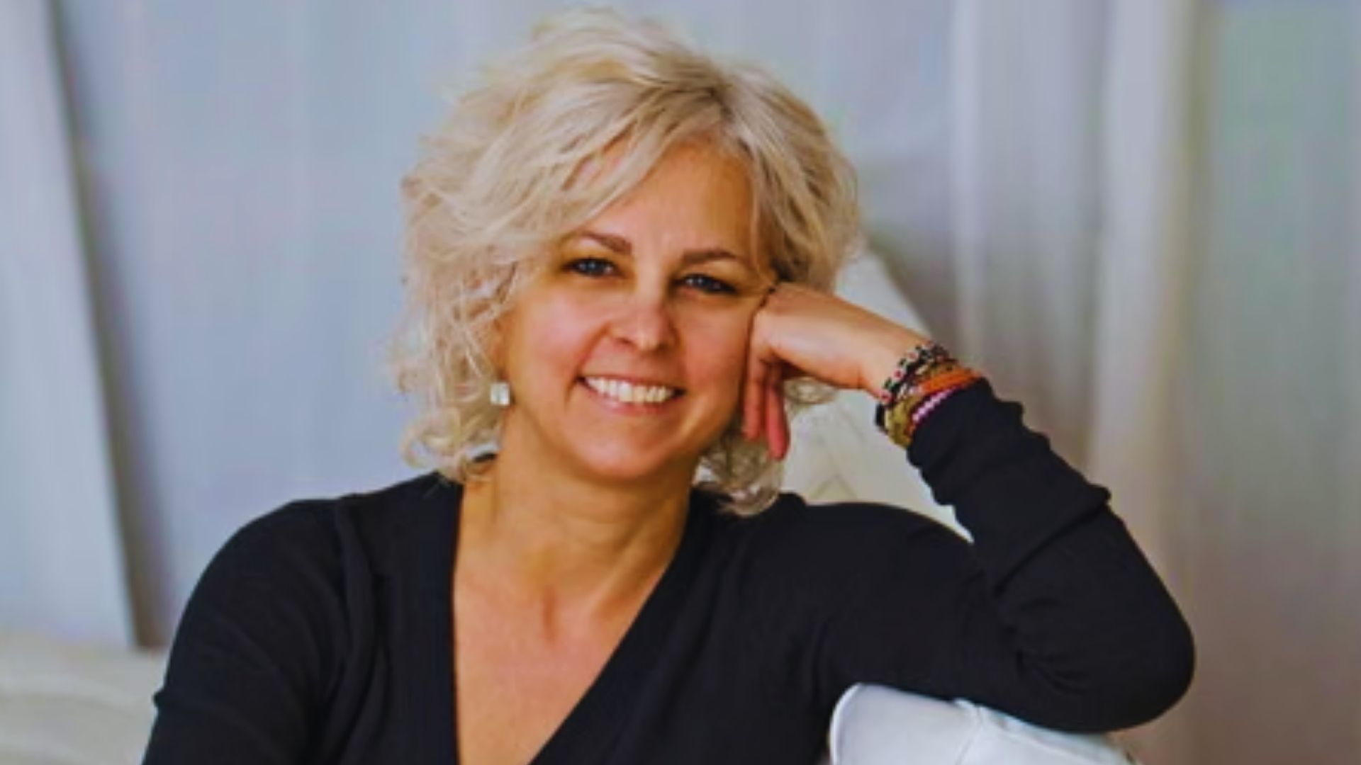 A woman with blonde hair is seated on a white couch, looking relaxed and comfortable in her surroundings.