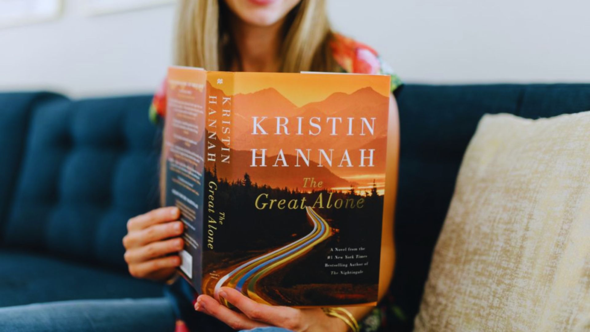 A woman holds a book titled "Kristin Hannah," showcasing her interest in the author's work.