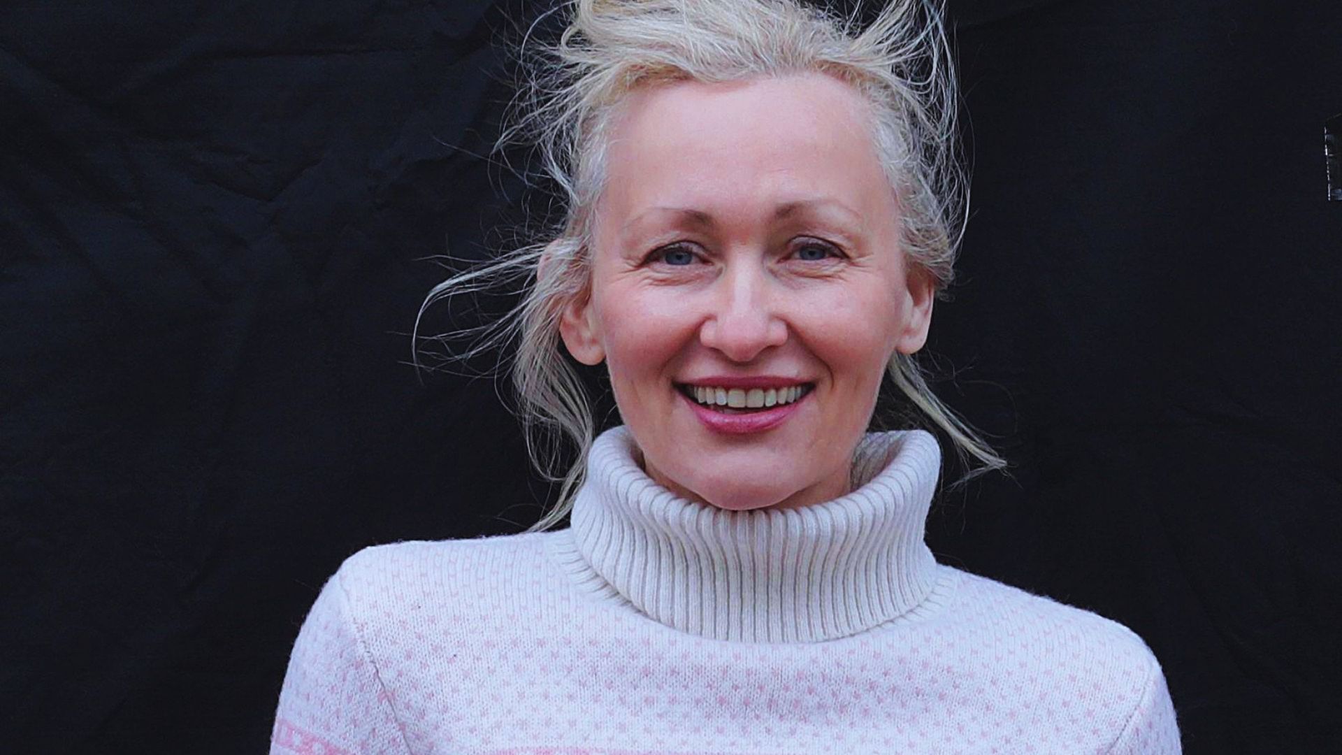 A woman wearing a pink sweater smiles warmly at the camera.
