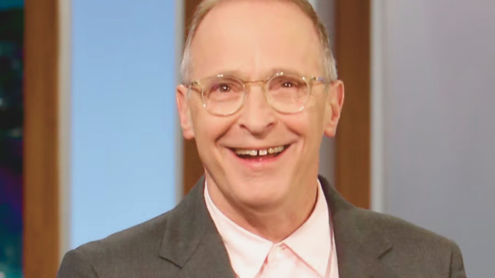 A smiling man wearing glasses and a pink shirt, exuding a friendly and approachable demeanor.