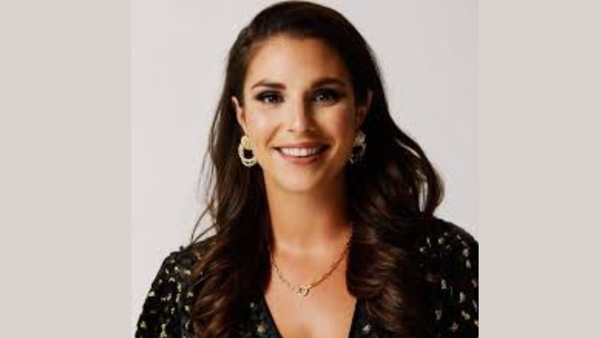 A woman with long hair wearing gold earrings, looking confidently at the camera.