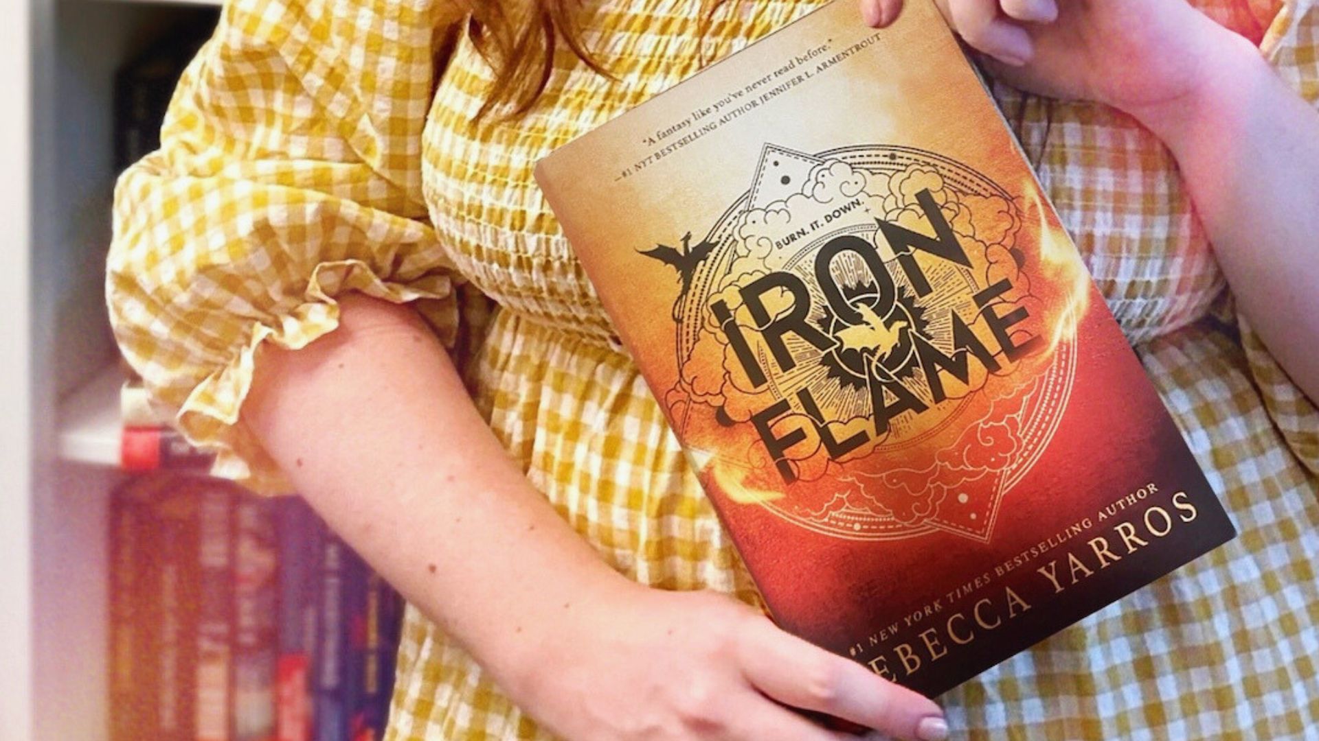 A woman holding a book titled "Iron Flame," showcasing her interest in literature.