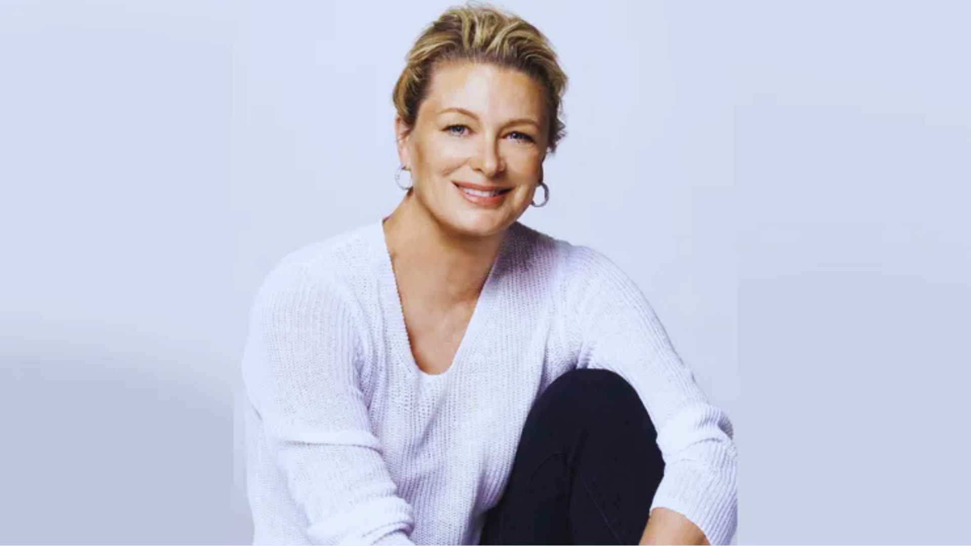 A woman wearing a white sweater is seated on a chair, looking relaxed and comfortable.