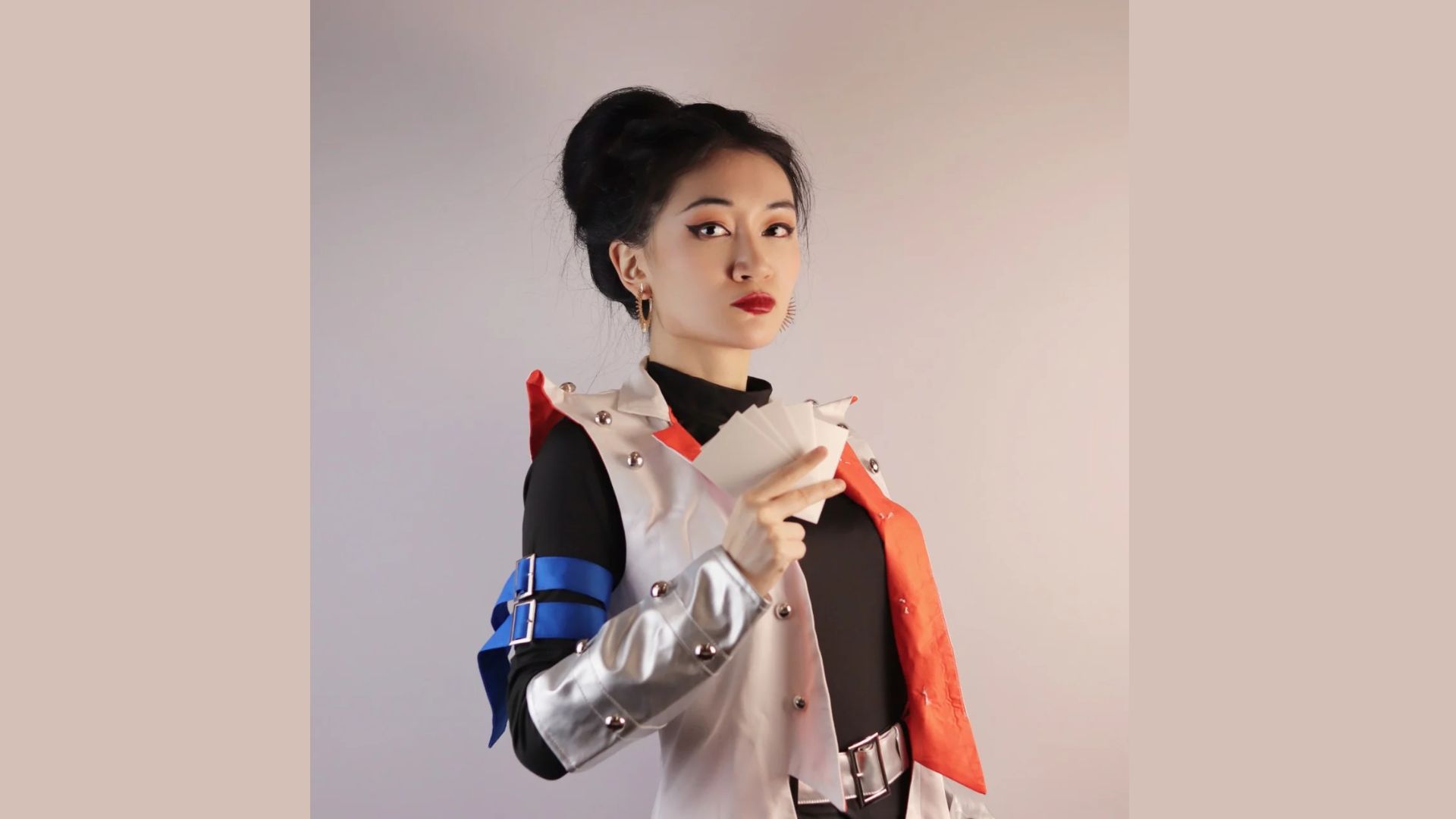 A woman in a costume holds a white and red card, smiling and posing for the camera.