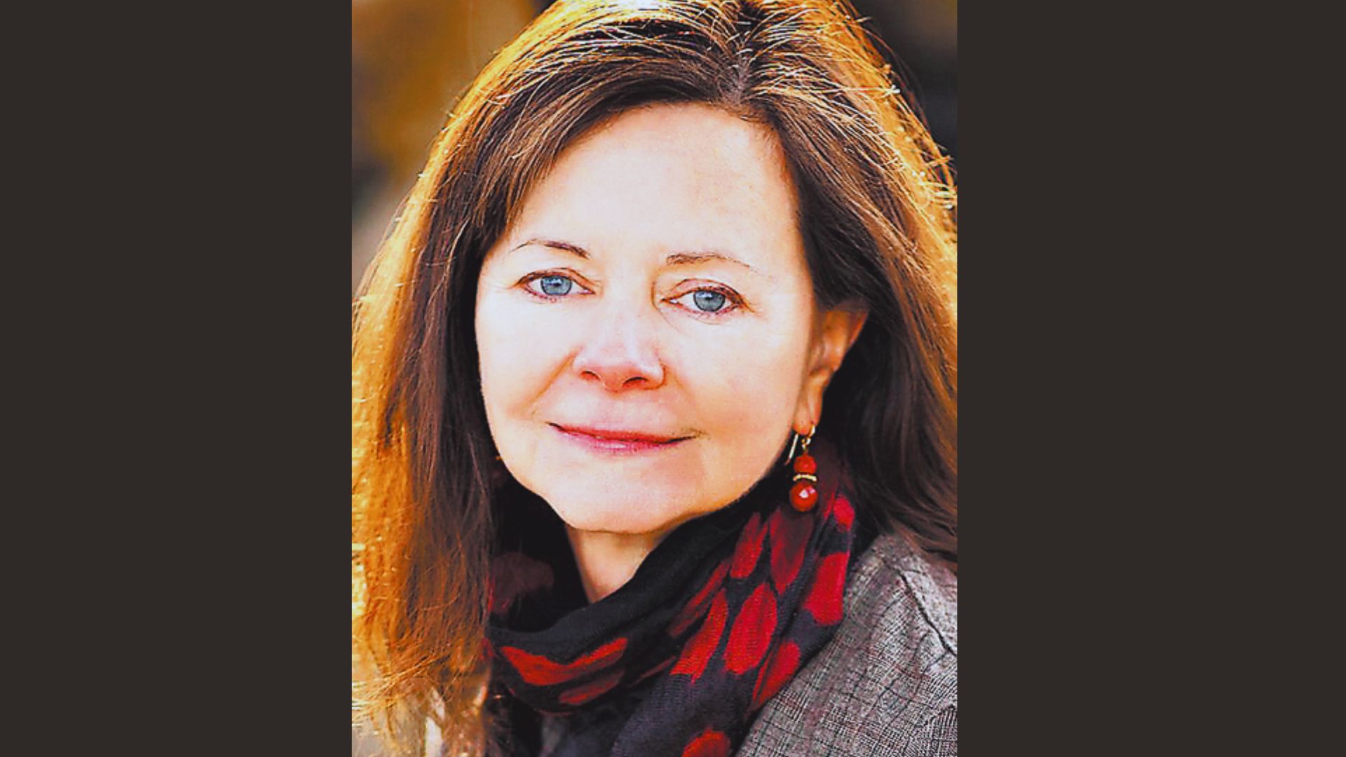 A woman with long brown hair wearing a red scarf, looking thoughtfully to the side.