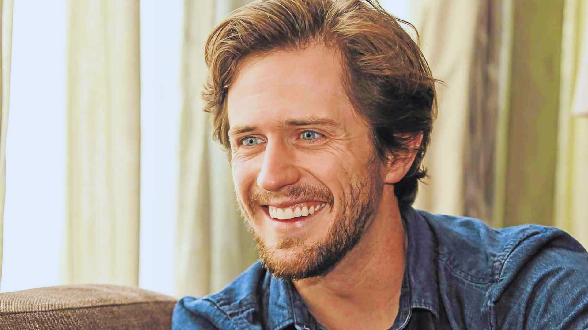 A smiling man with a beard wearing a blue shirt, exuding a friendly and approachable demeanor.