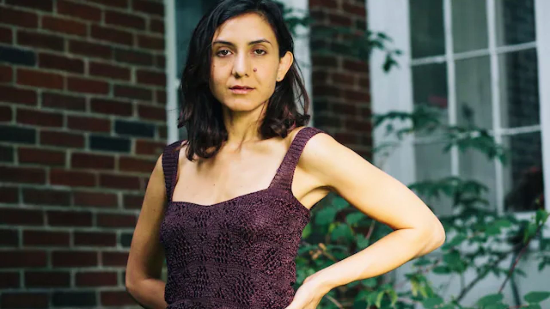 Outside, a woman in a purple dress stands confidently, representing Ottessa Moshfegh, author of "My Year of Rest and Relaxation."
