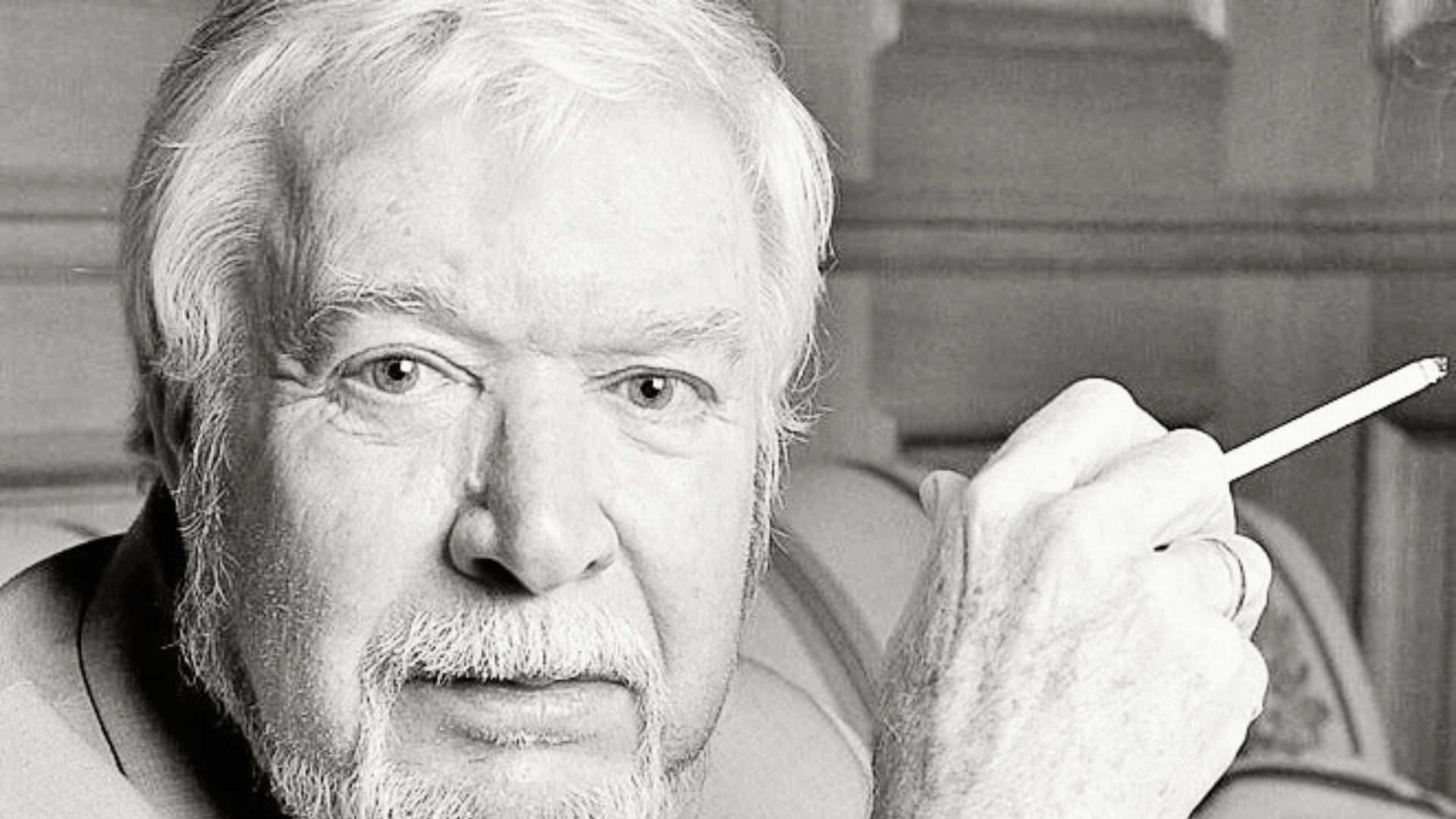 Timothy Findley with a white beard is smoking a cigarette, reflecting a contemplative mood.