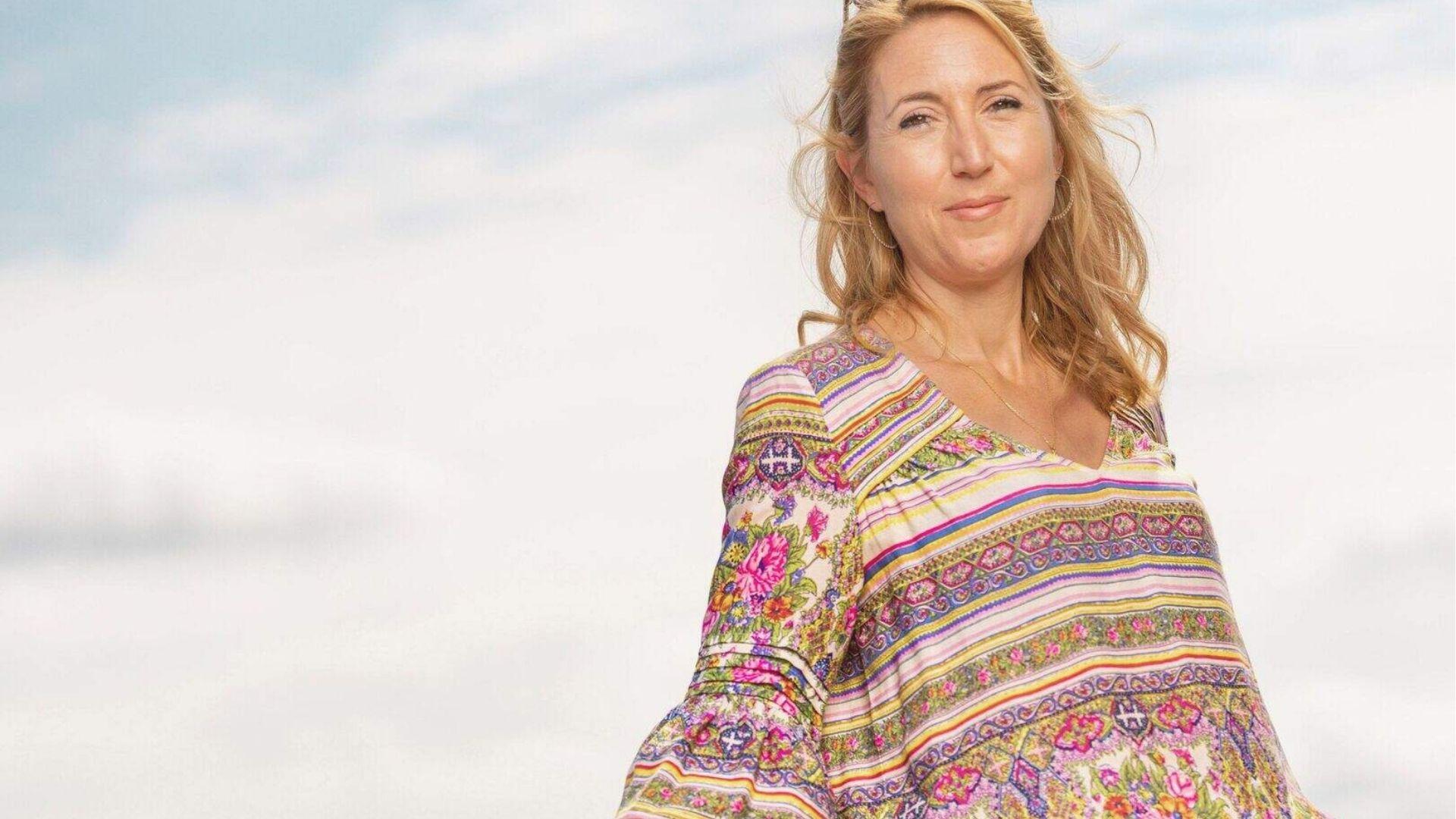 Bestselling thriller author Lisa Jewell stands outdoors against a soft cloudy sky, wearing a colorful floral striped blouse.