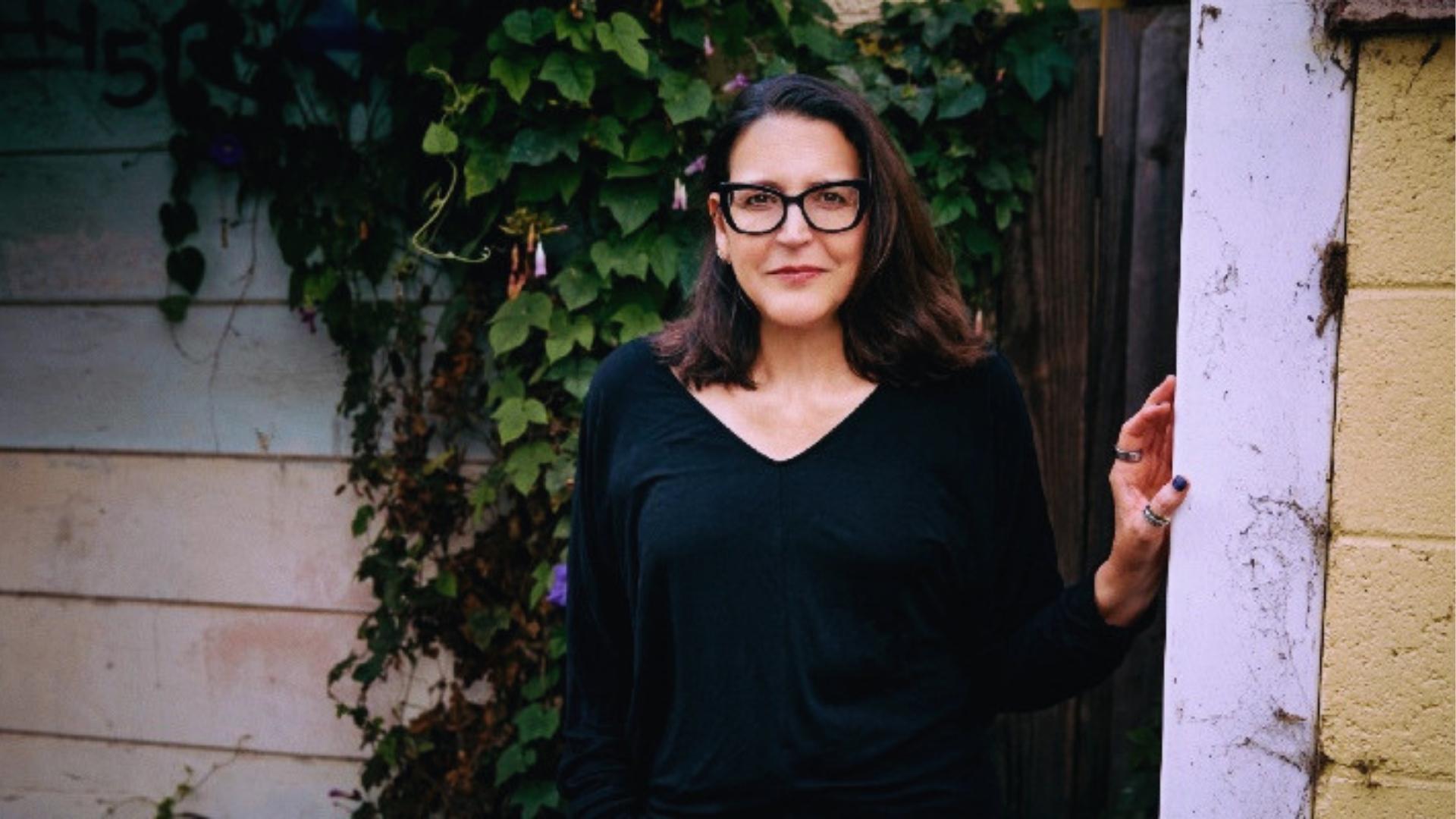 Author photo of Julie Clark wearing black V-neck top and glasses, standing outdoor