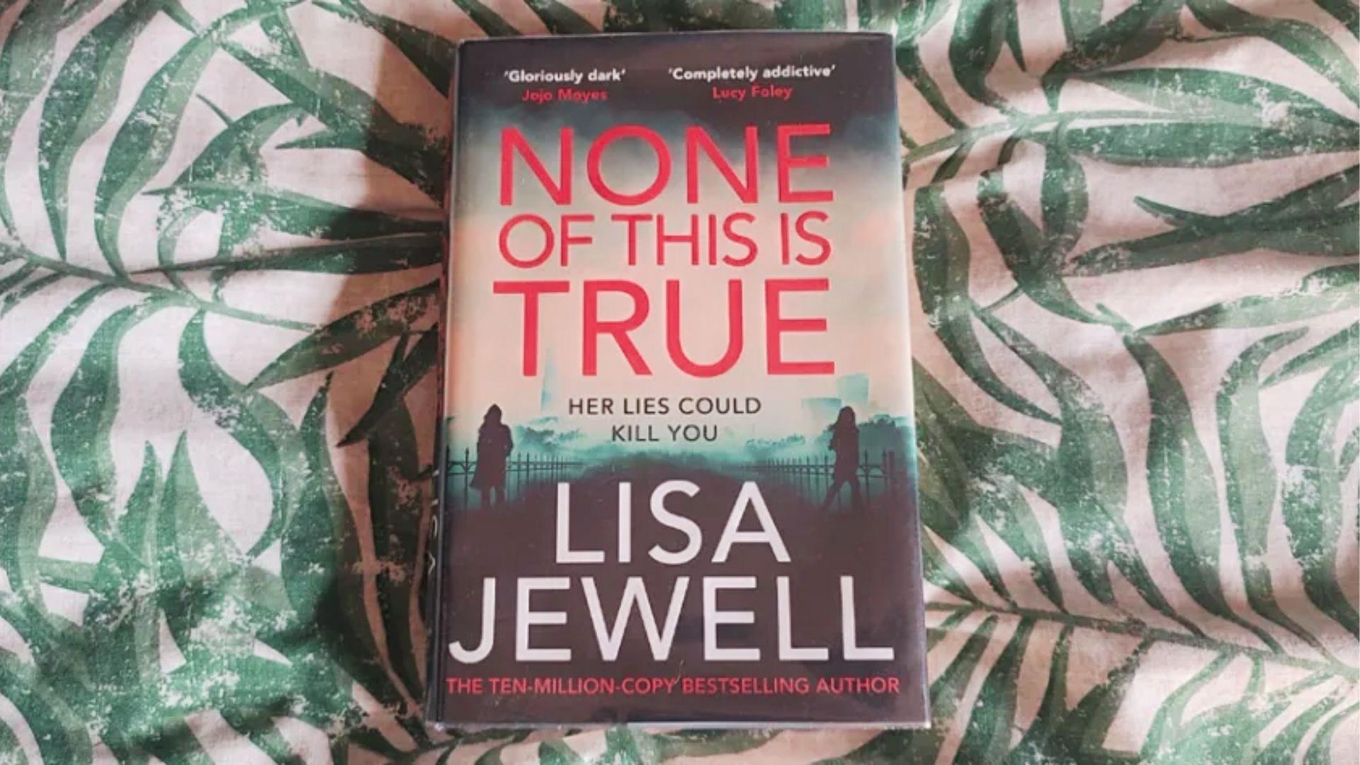 Hardcover edition of None of This Is True by Lisa Jewell lies flat on green and white leaf-patterned fabric.
