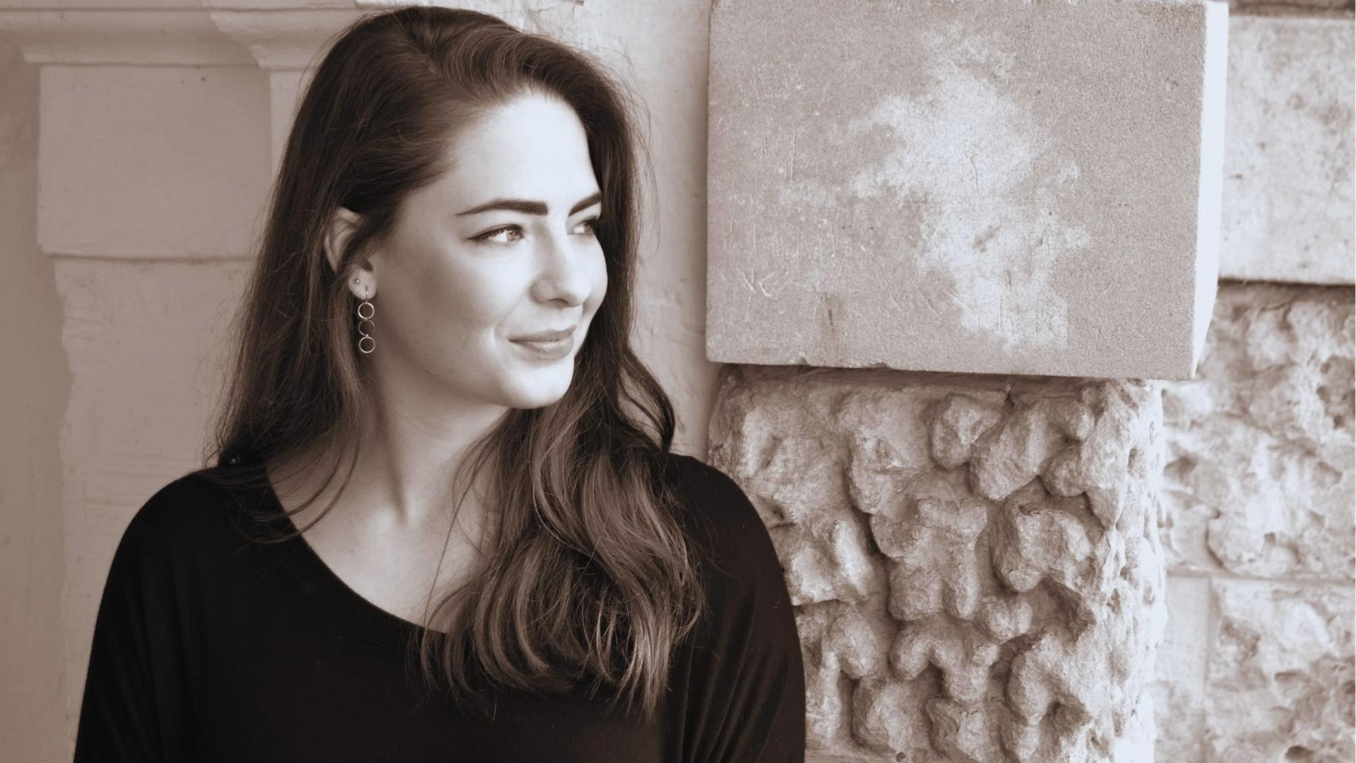 Sepia-toned author photo of M. L. Rio with long wavy hair and hoop earrings, smiling beside stone wall