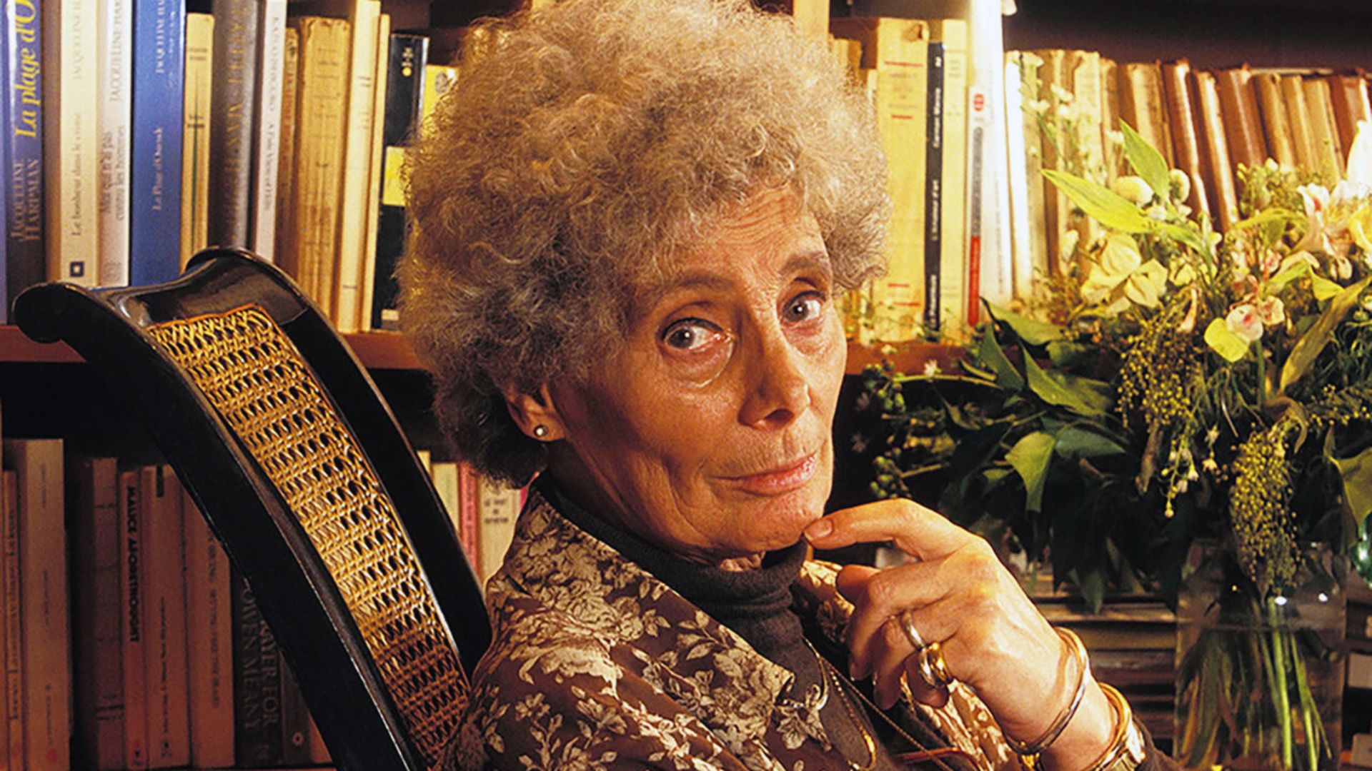 Jacqueline Harpman, author of "I Who Have Never Known Men," poses in a floral dress with striking red lipstick.