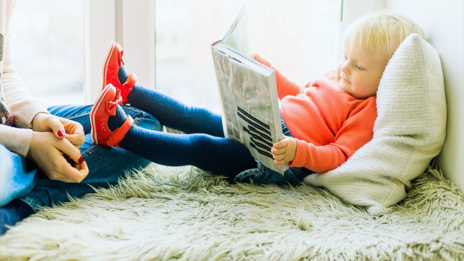 A woman and child sit on a rug, happily reading a book together.