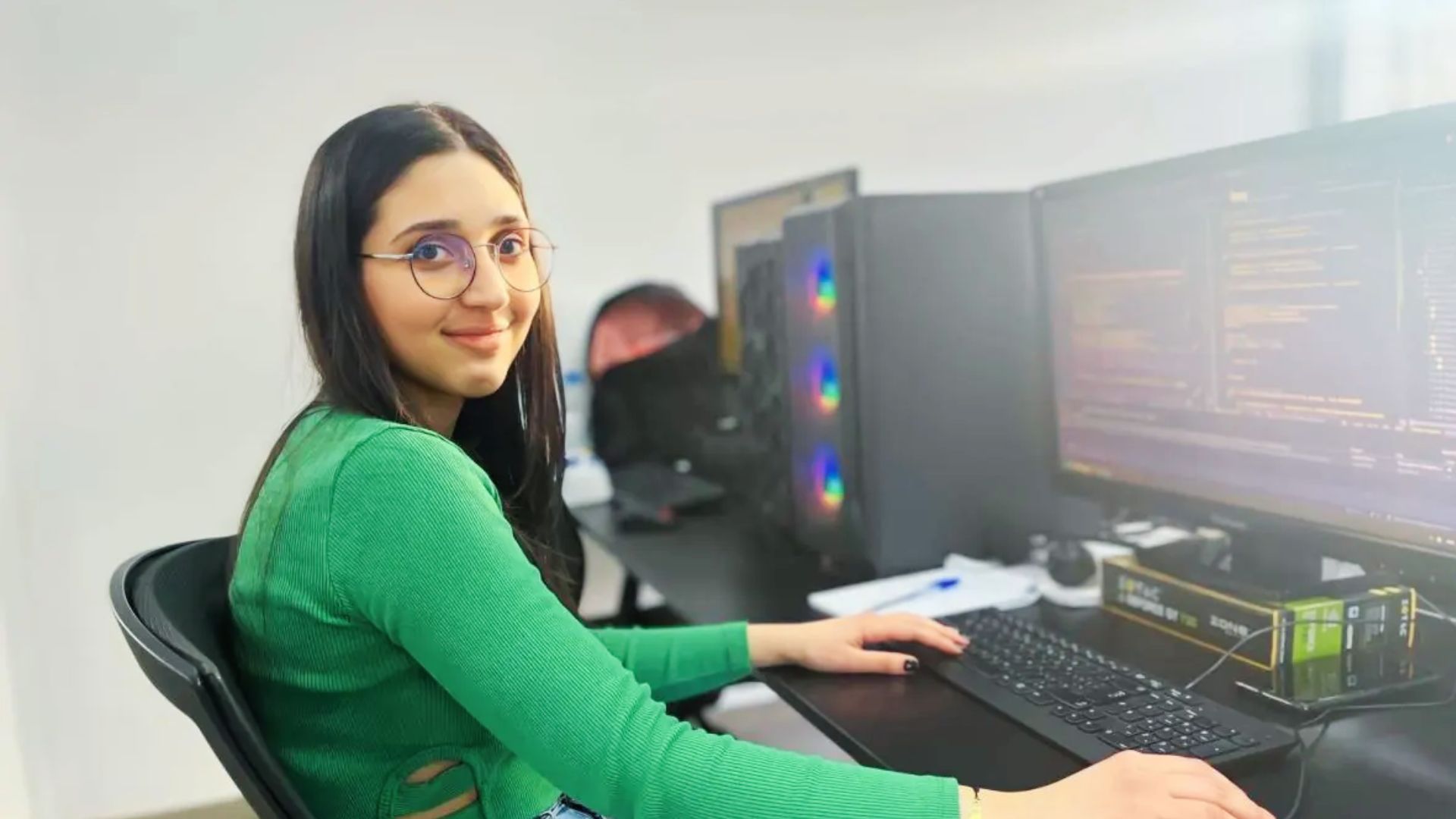 A woman in glasses works at her desk with a computer, reflecting on her personal story of becoming a software engineer.