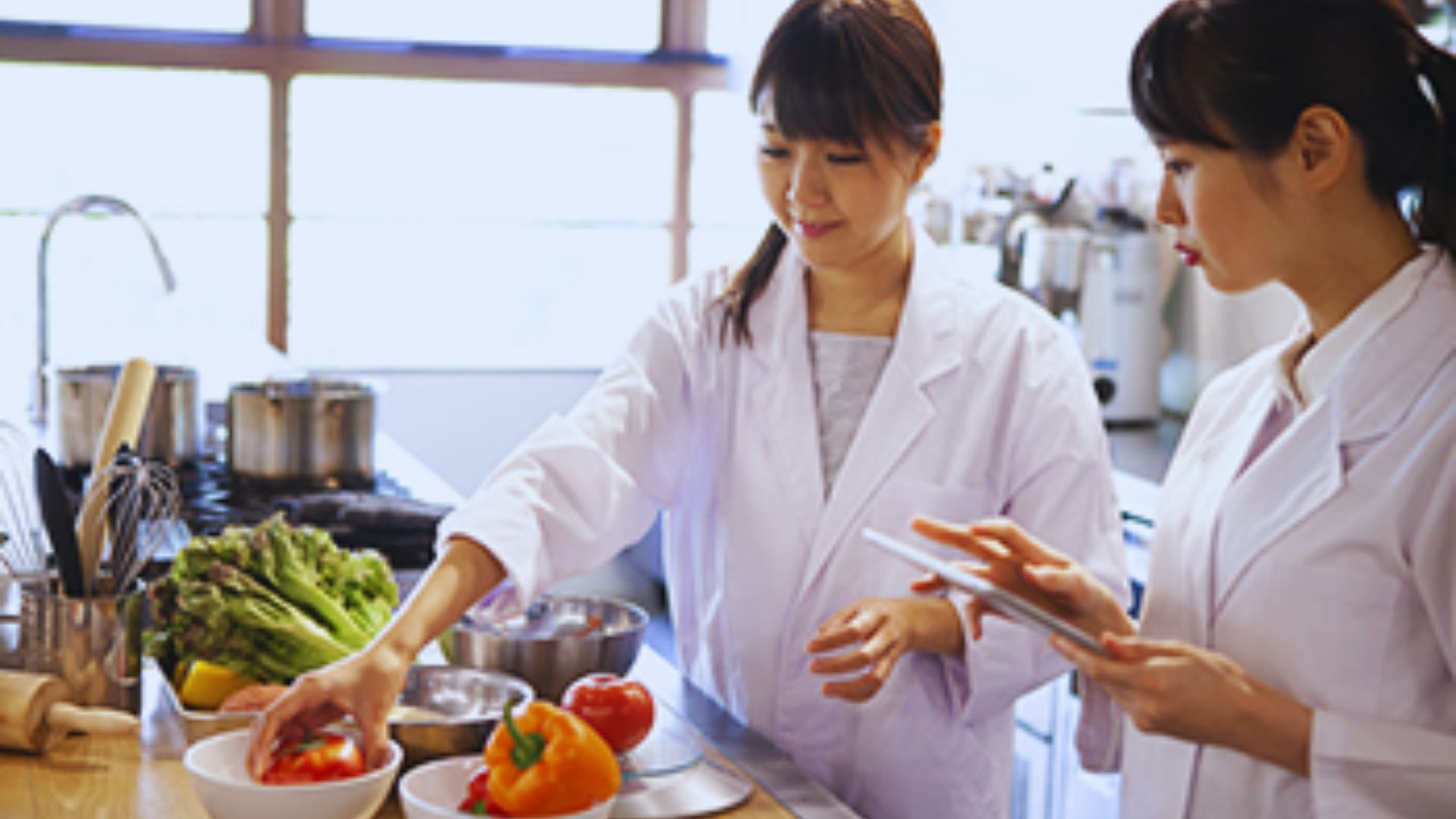 Two girls working together in a kitchen, preparing food with red capsicum.