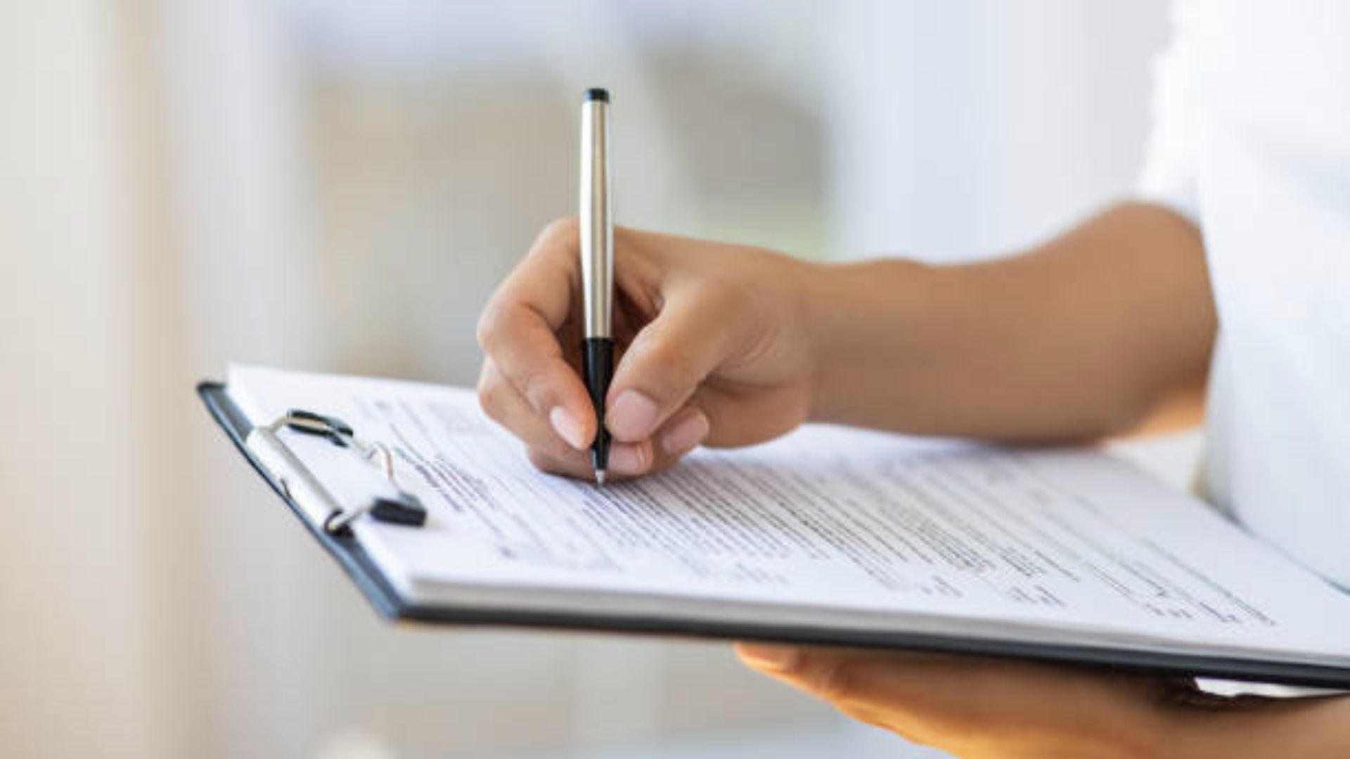 A woman's hand writing notes in a notepad, showcasing her focused expression and the pen in motion.