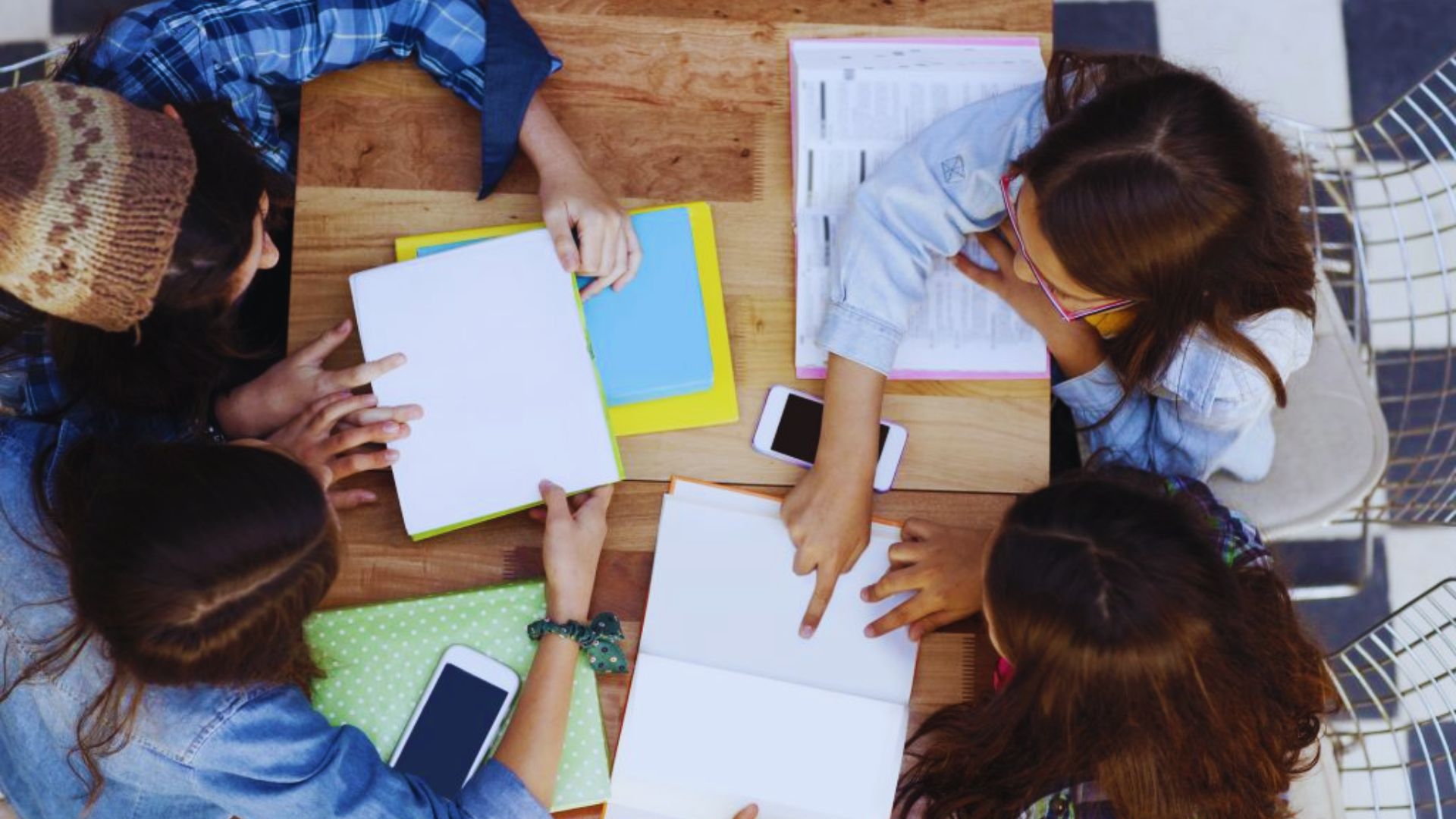 Four students studying together, viewed from above, with open books placed at the center.