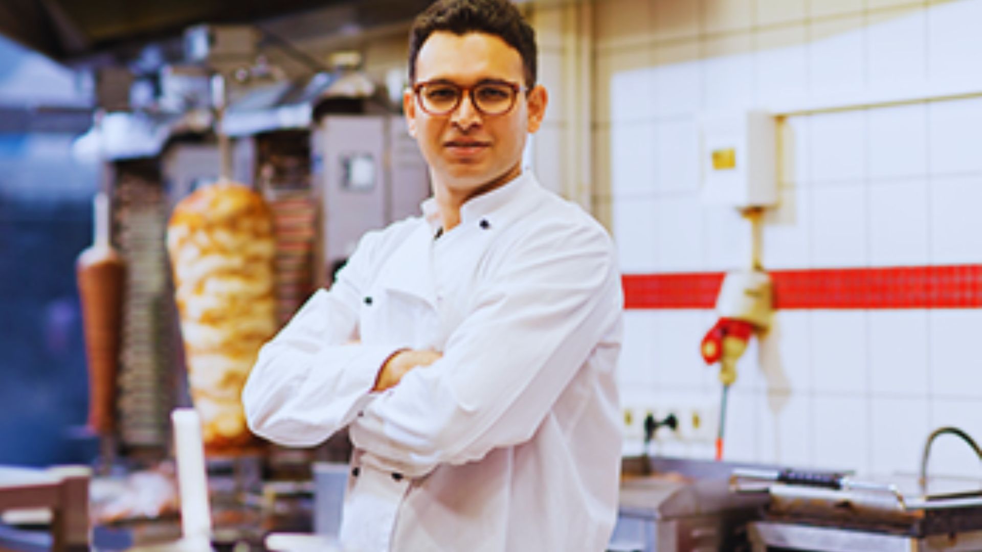 A chef wearing glasses, looking directly at the camera in a kitchen setting.