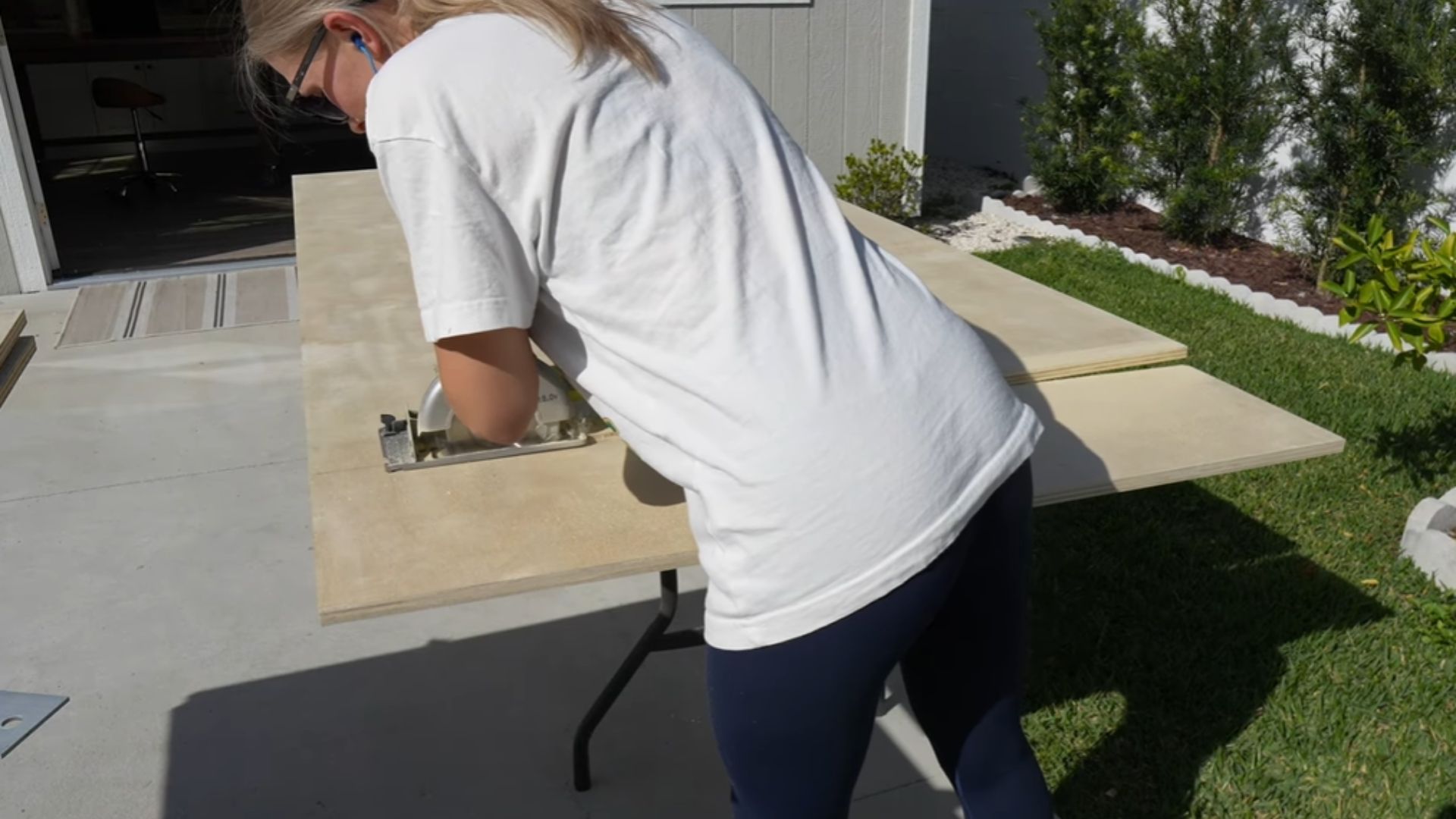 "A woman is using a saw to cut a piece of wood on a work table."