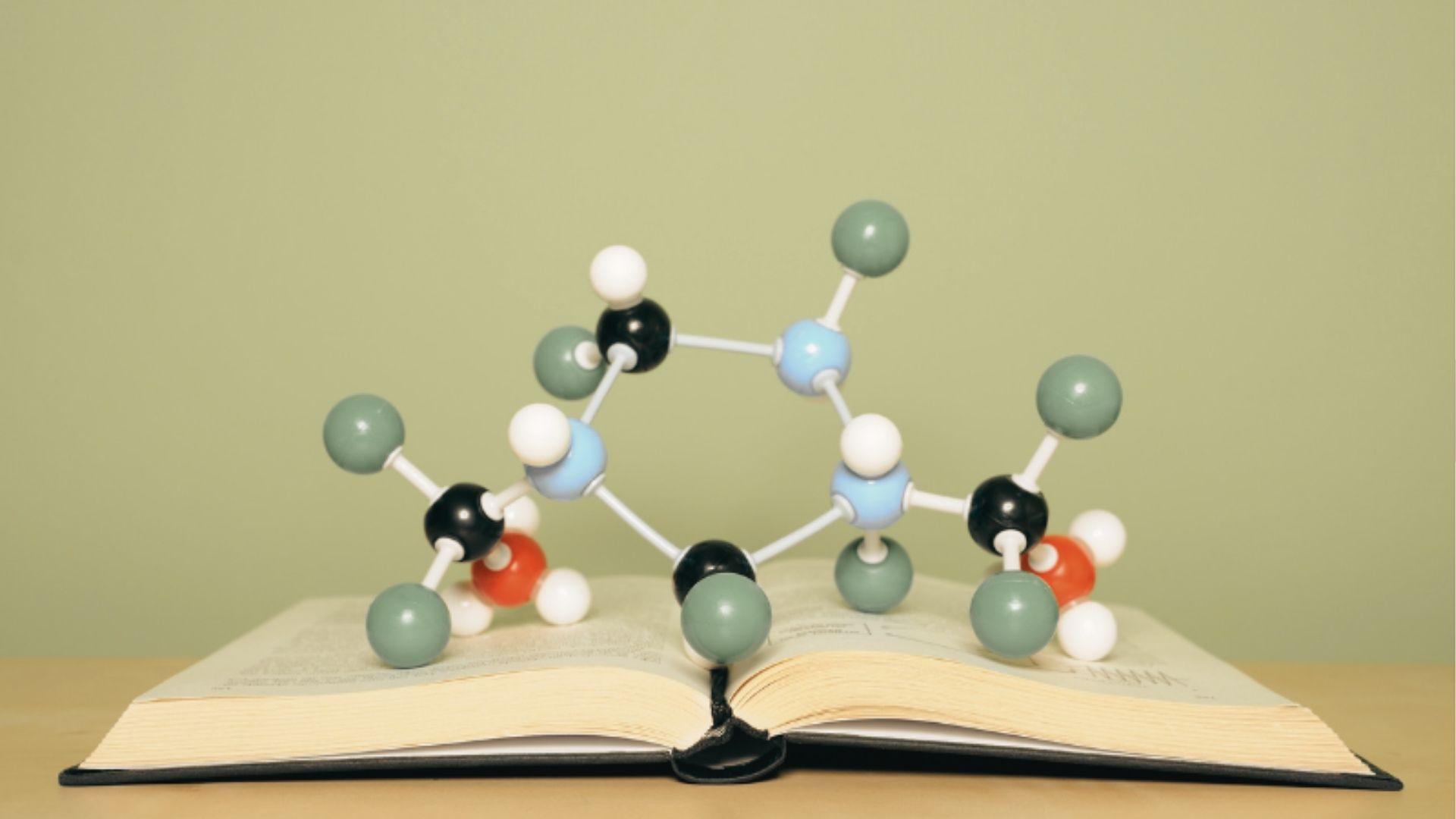 A colorful molecular model sits on top of an open textbook against a green background.