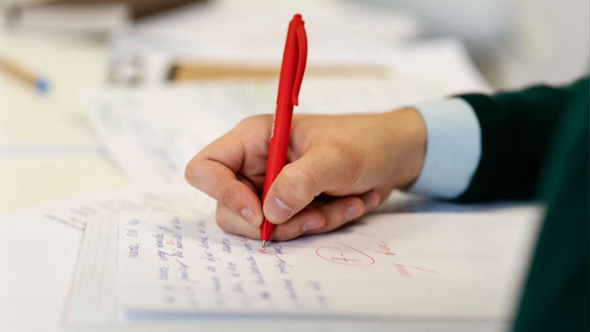 Student holds red pen while writing on paper, showing regular handwriting practice builds accuracy.