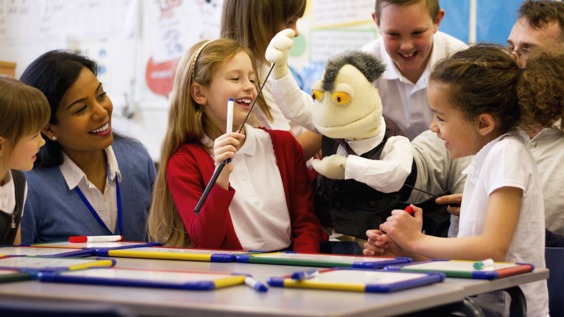 Students laugh with their teacher as they use a puppet during a classroom activity.