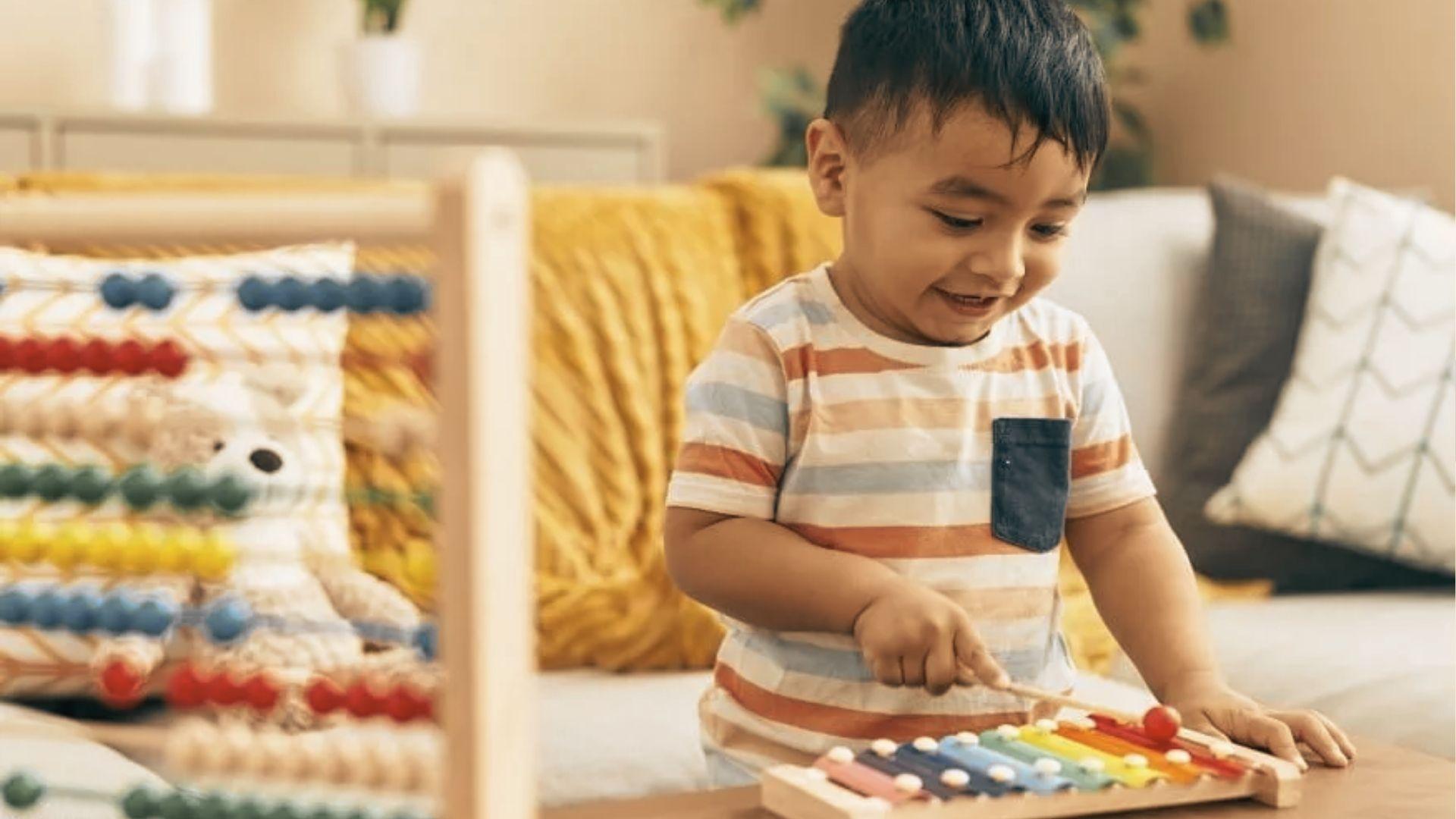 A smiling toddler plays a colorful xylophone with a mallet while an abacus sits nearby.