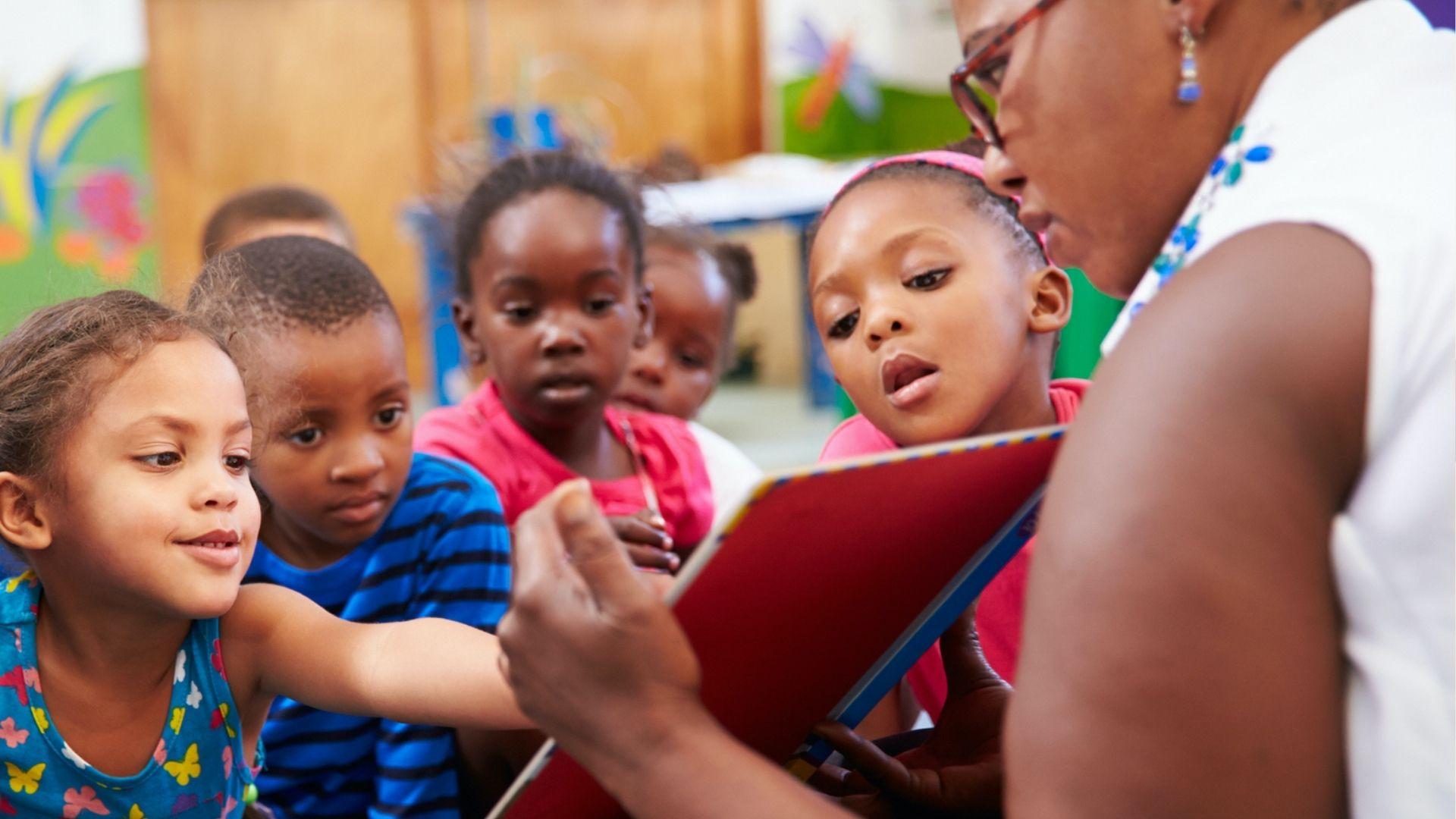 Teacher reads a picture book to a group of engaged preschool children sitting in a circle.